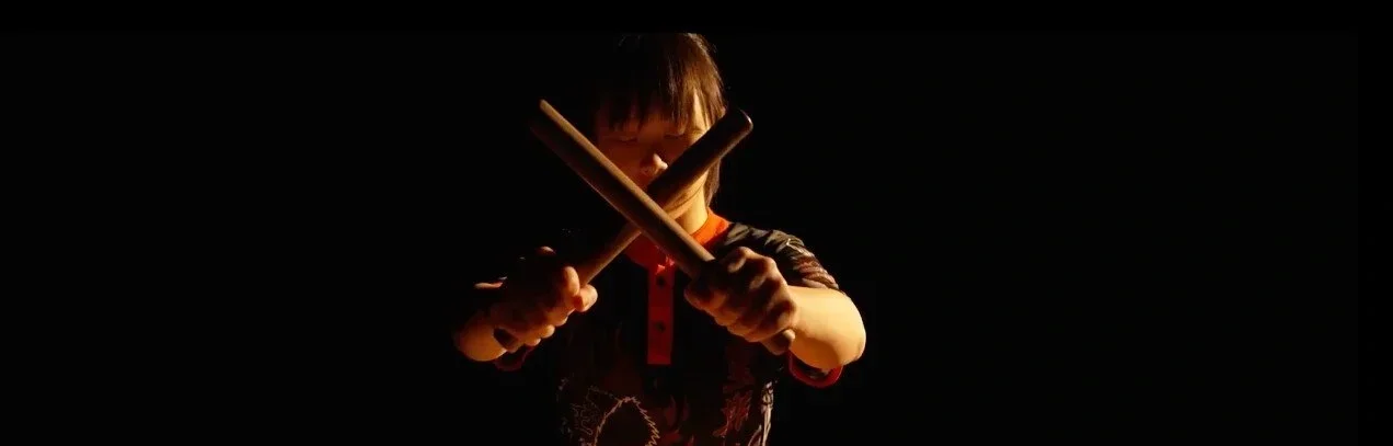Child practicing martial arts with wooden sticks in a dark setting