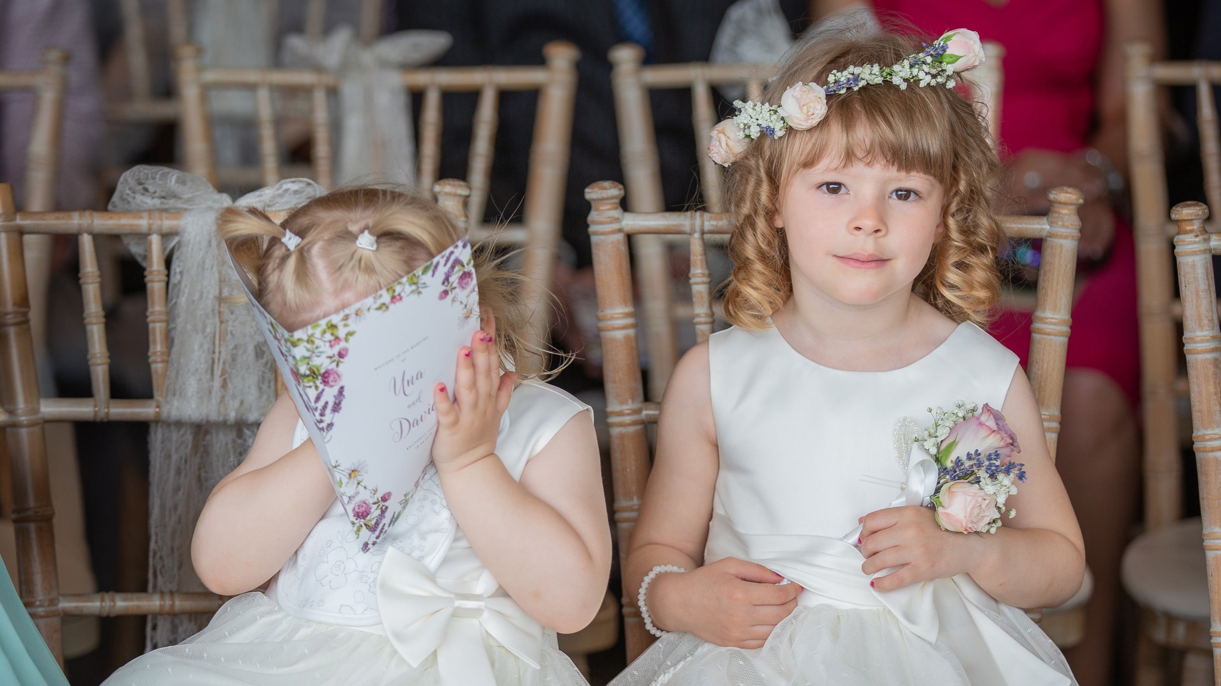 A wedding party standing outdoors on a grassy lawn with trees in the background, holding hands and celebrating.