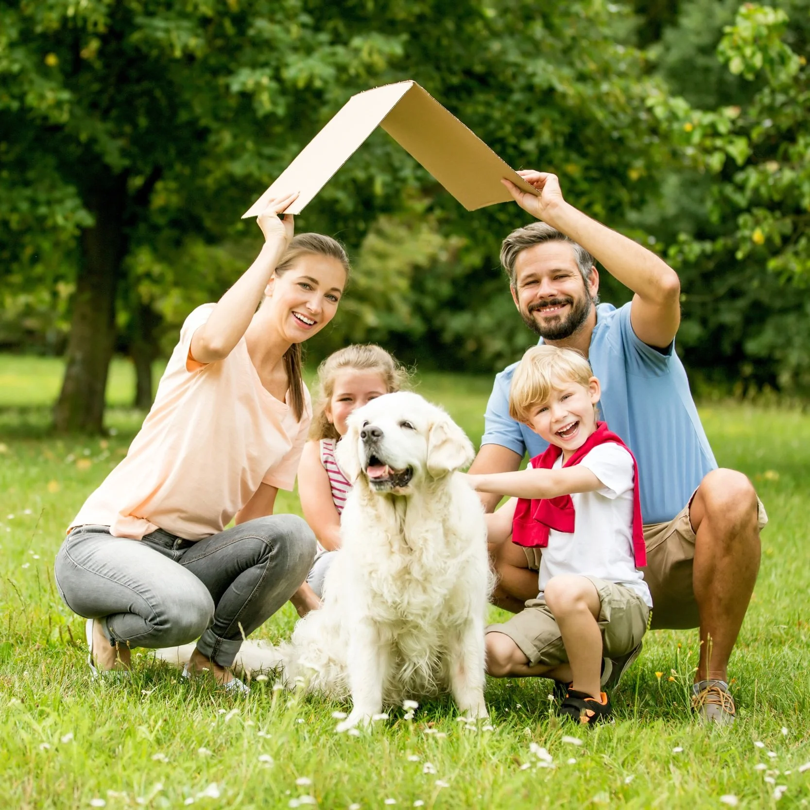 Une famille avec un chien Golden Retriever souriant, dehors dans un parc, jouant avec une boîte en carton au-dessus d'eux, sous un ciel clair.