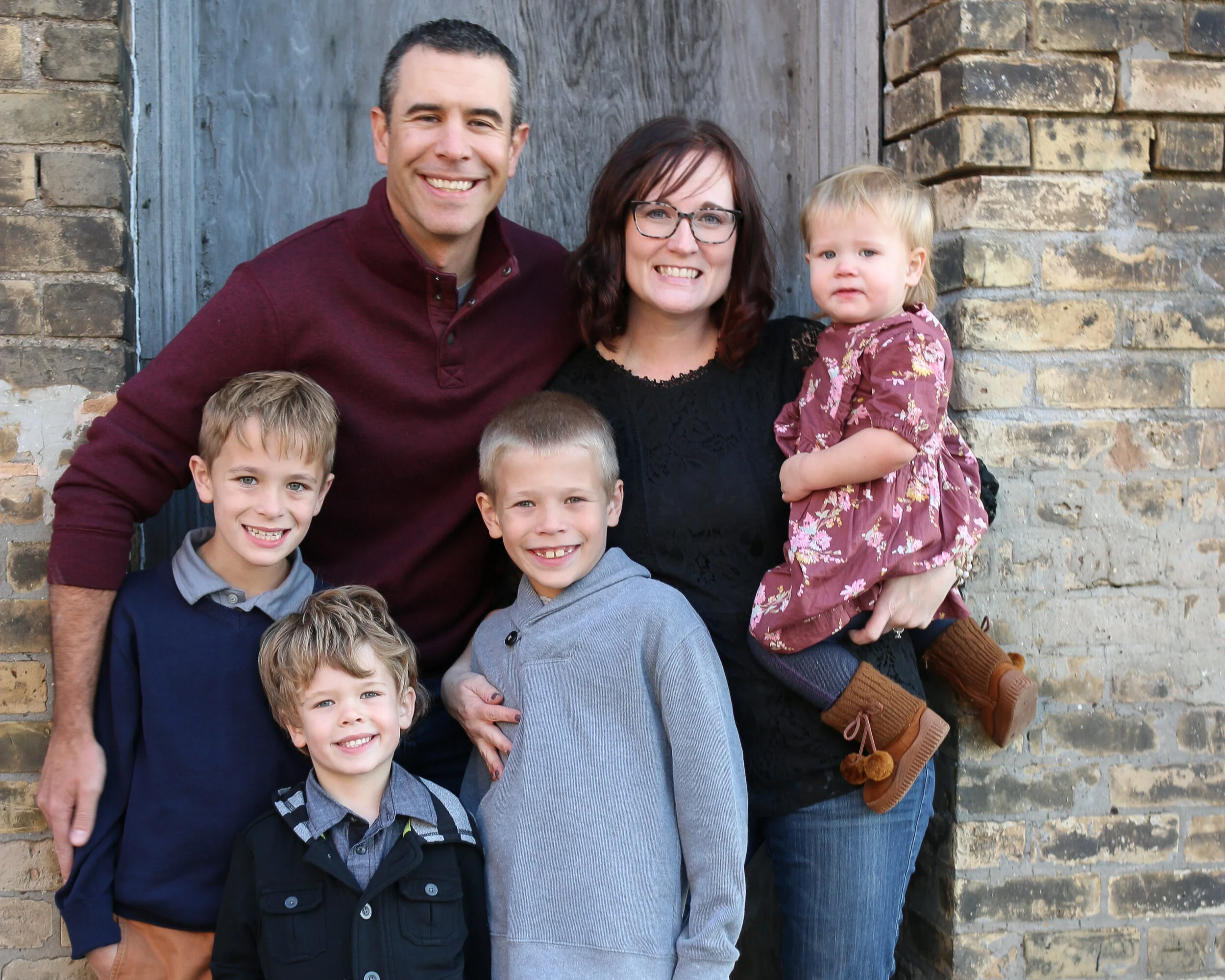 Amy, her husband, and her four children — four blessings after struggling with infertility and miscarriage — pose for a family photo in front of a brick and wood background.