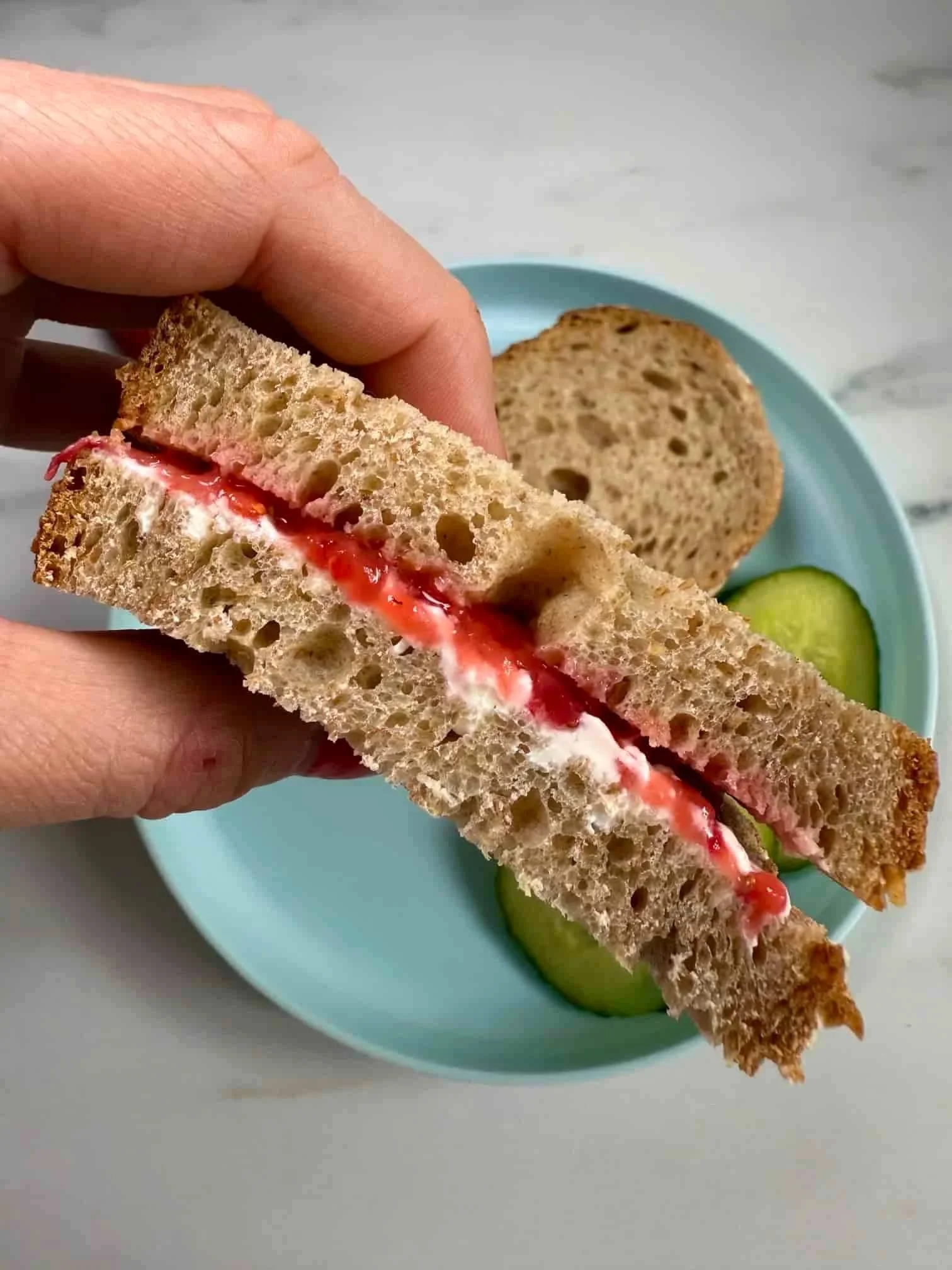 Slices of bread sandwiched together with smashed strawberries and cream cheese and served with slices of cucumber