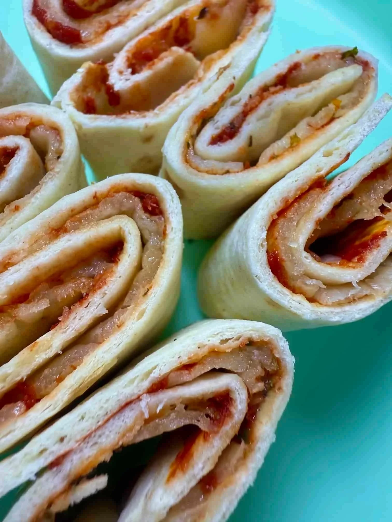 Several tortilla pizza roll-ups, sliced and standing on serving dish