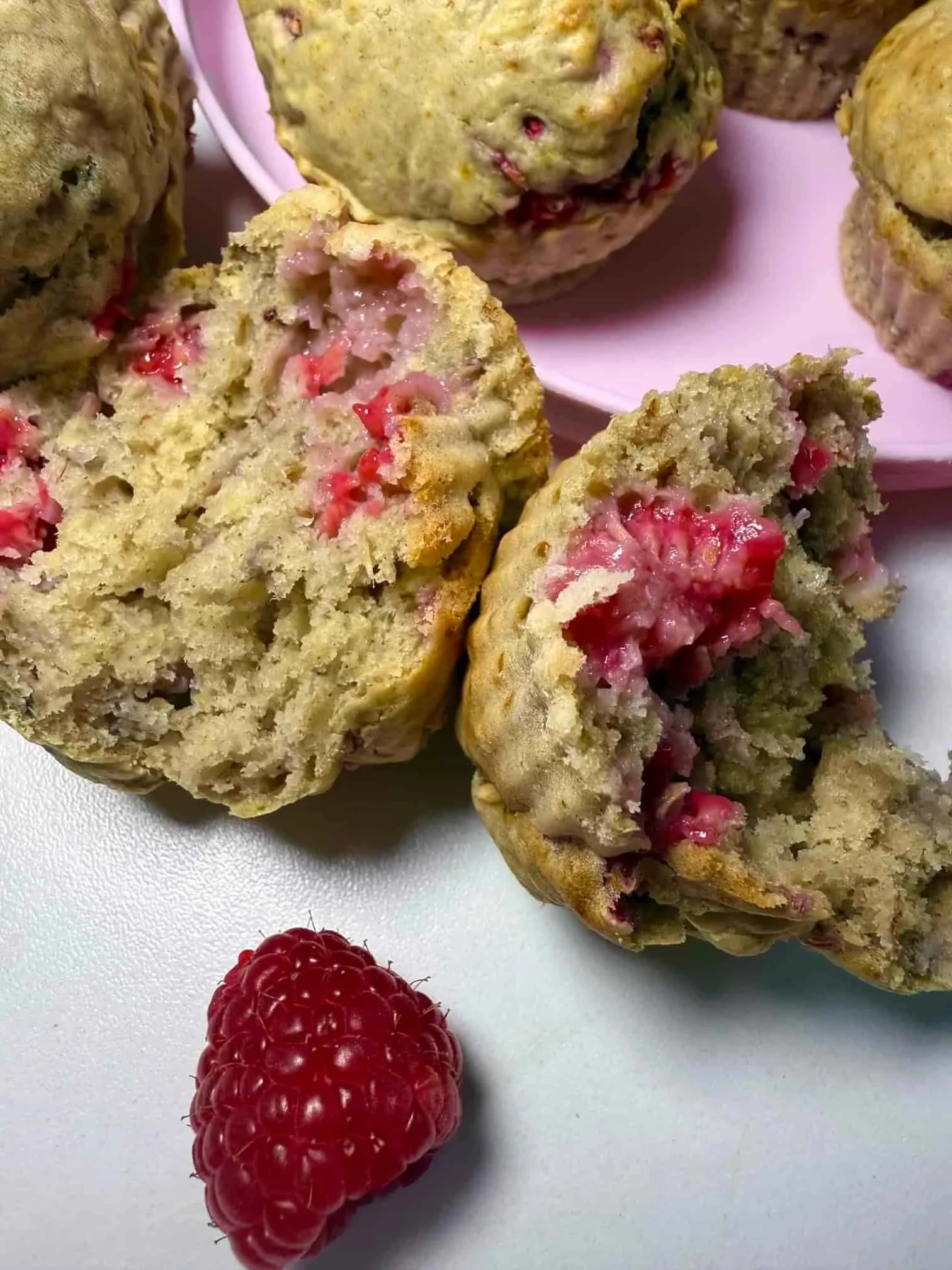 Several baked raspberry muffins served on pink toddler plate with one muffin cut in half