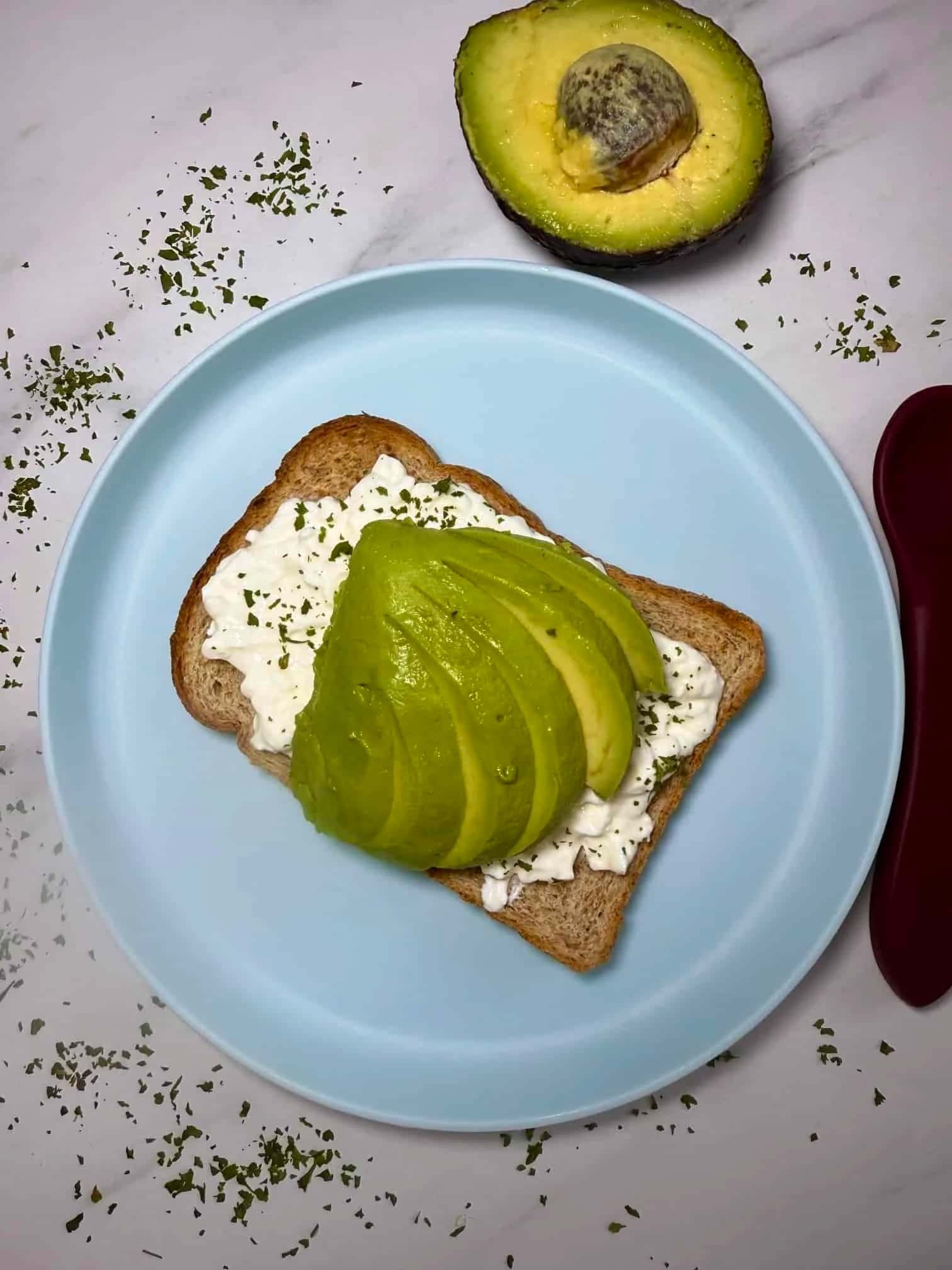 A close up image of slices of avocado on top of toast spread with cottage cheese and herbs