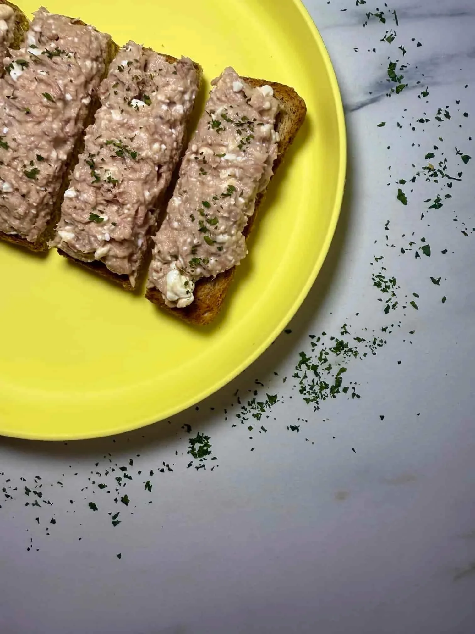 A tuna and cottage cheese topping spread on toast, garnished with parsley and served on toddler plate