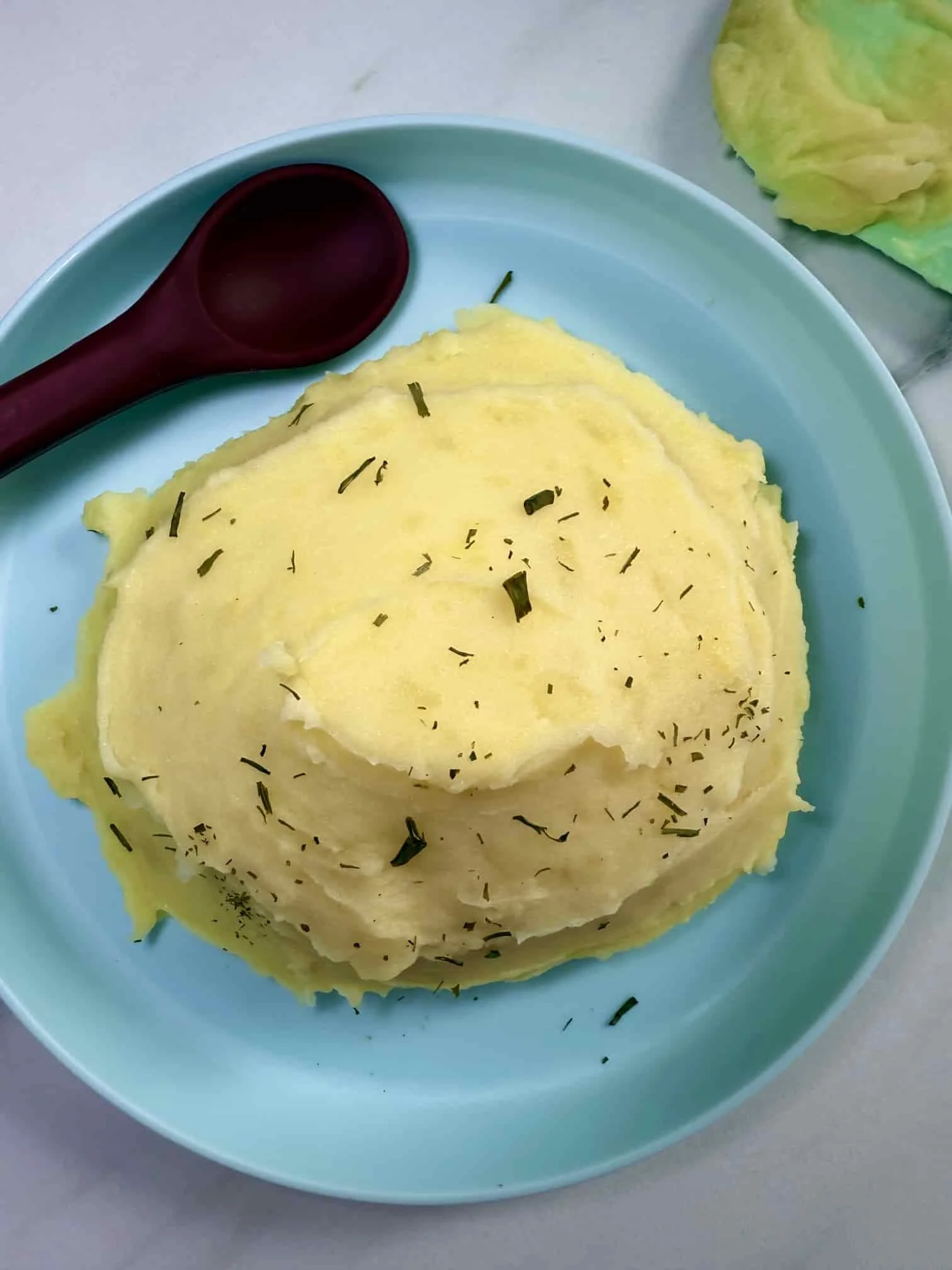 A serving of homemade mashed potato on a toddler plate sprinkled with chives