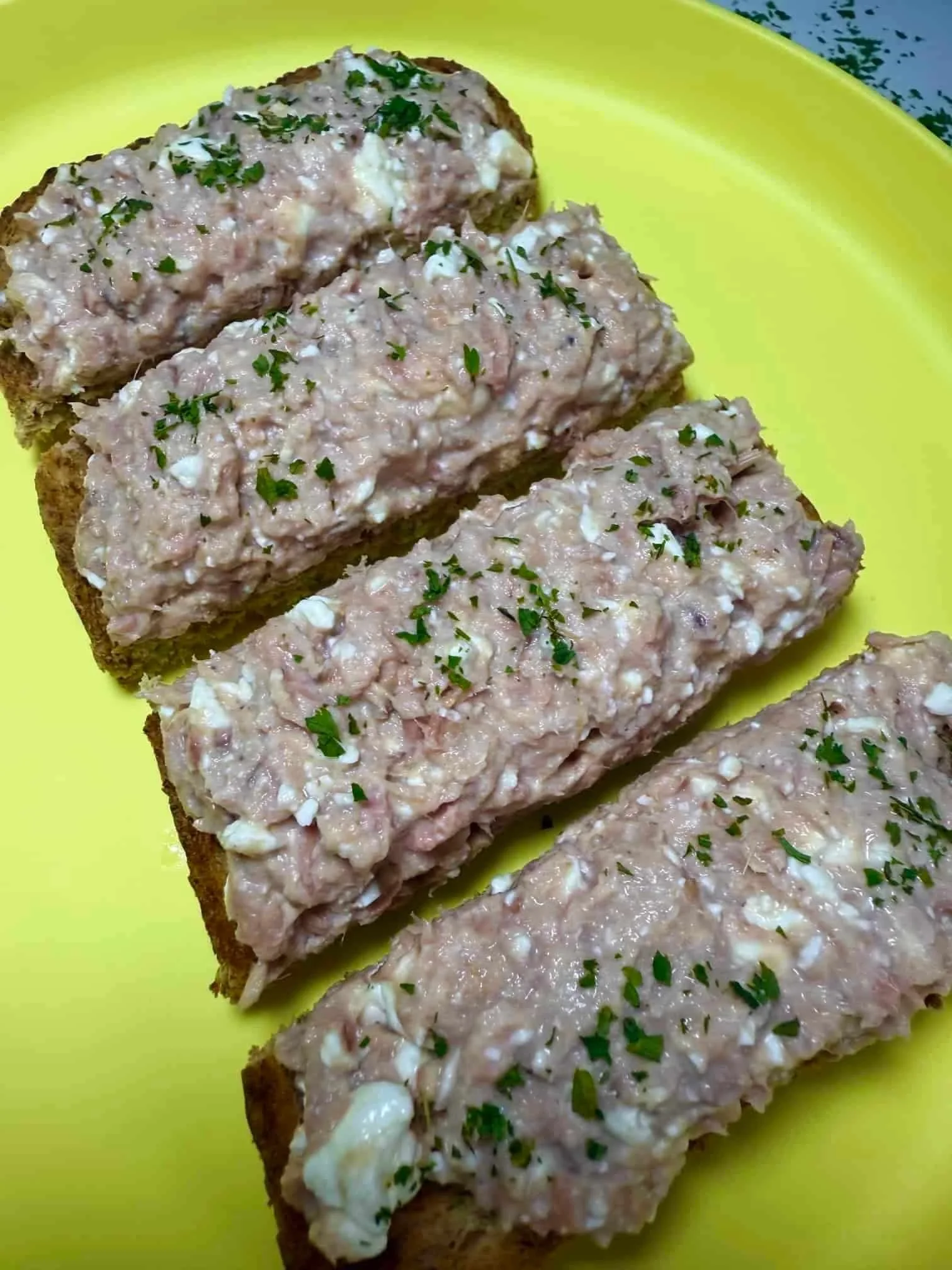 A tuna and cottage cheese topping spread on toast, garnished with parsley and served on toddler plate