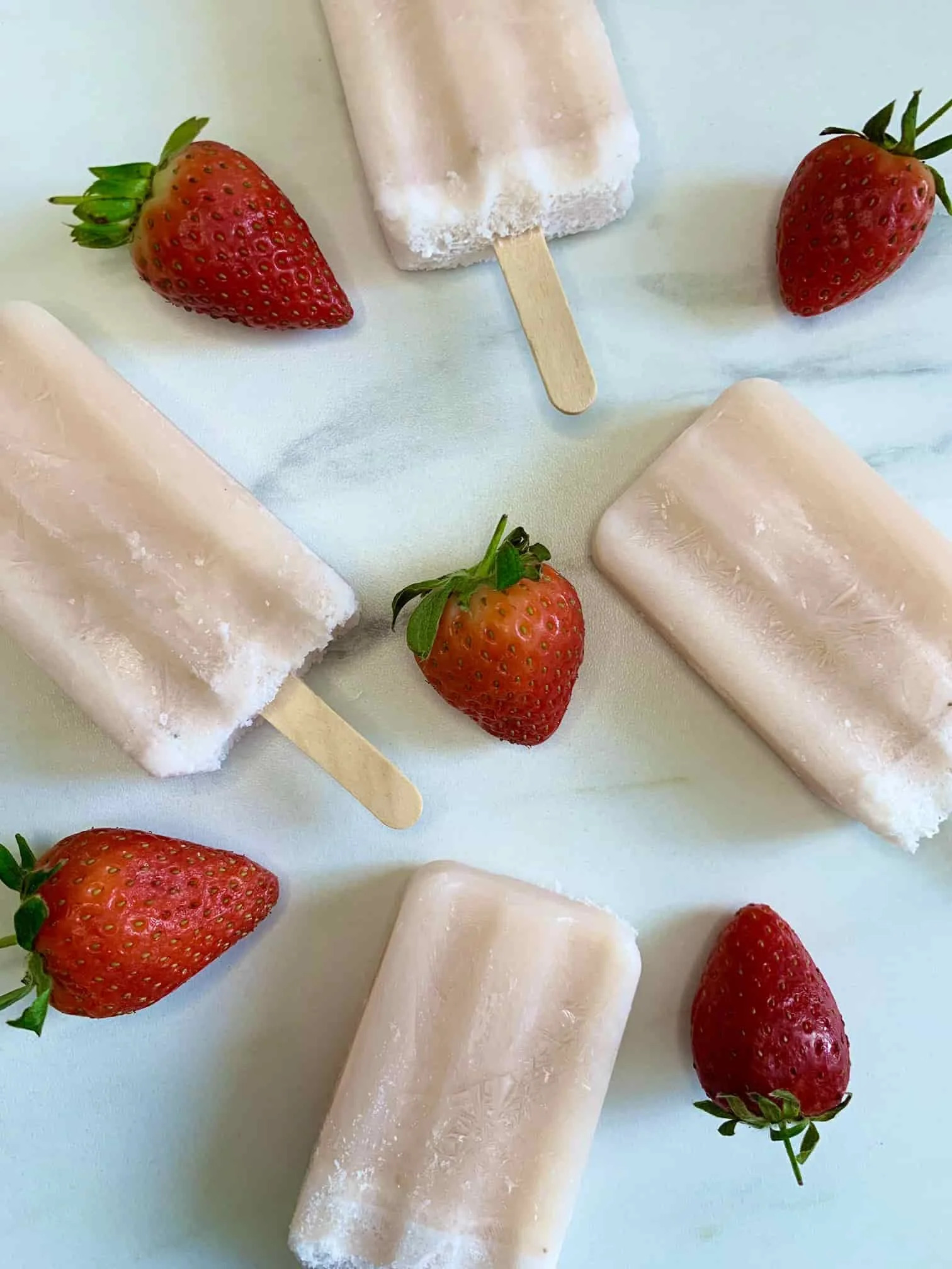 Four frozen milk lollies displayed on marble board and served with whole strawberries
