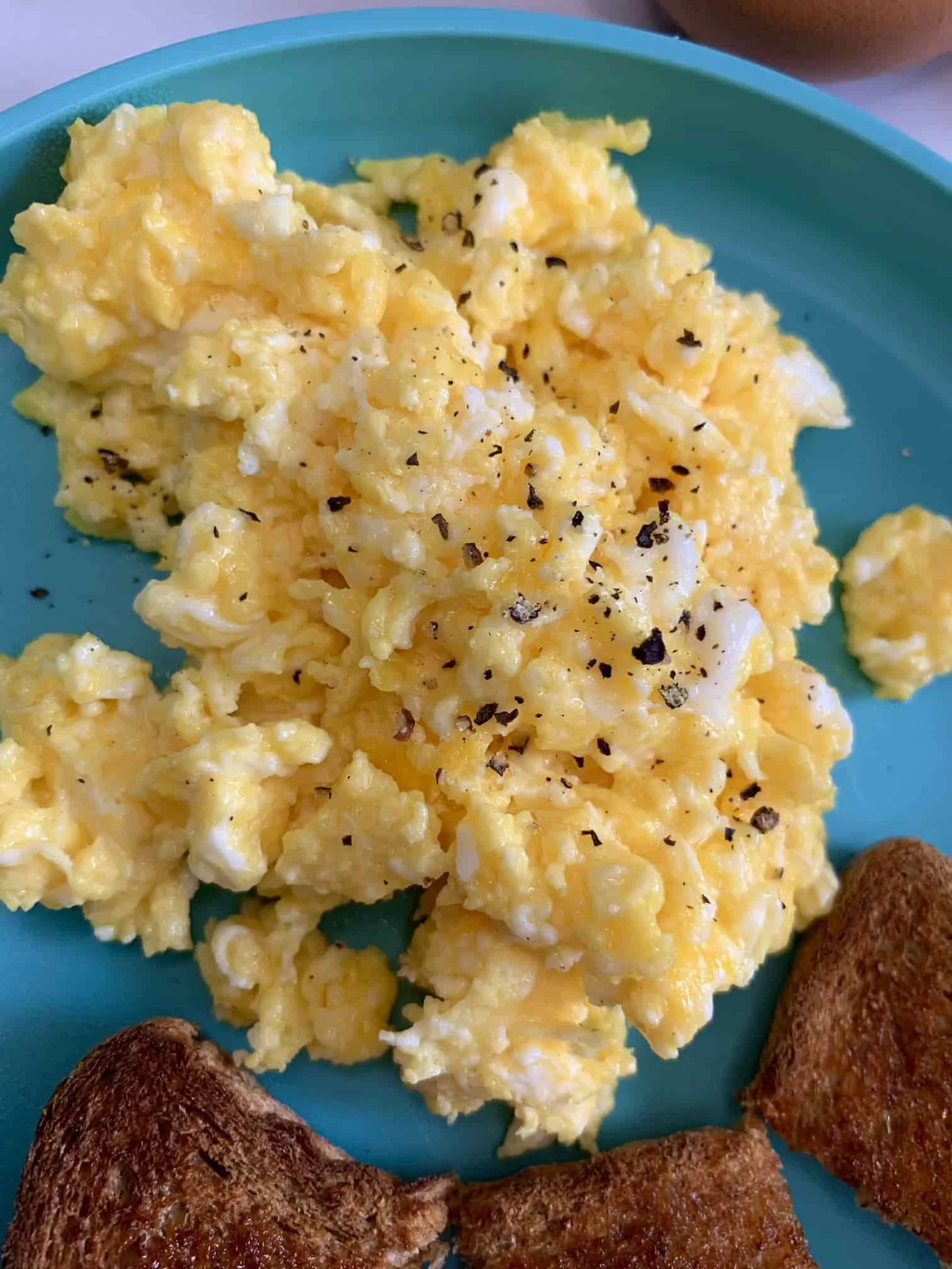 A serving of cooked scrambled egg on toddler plate served with pieces of toast