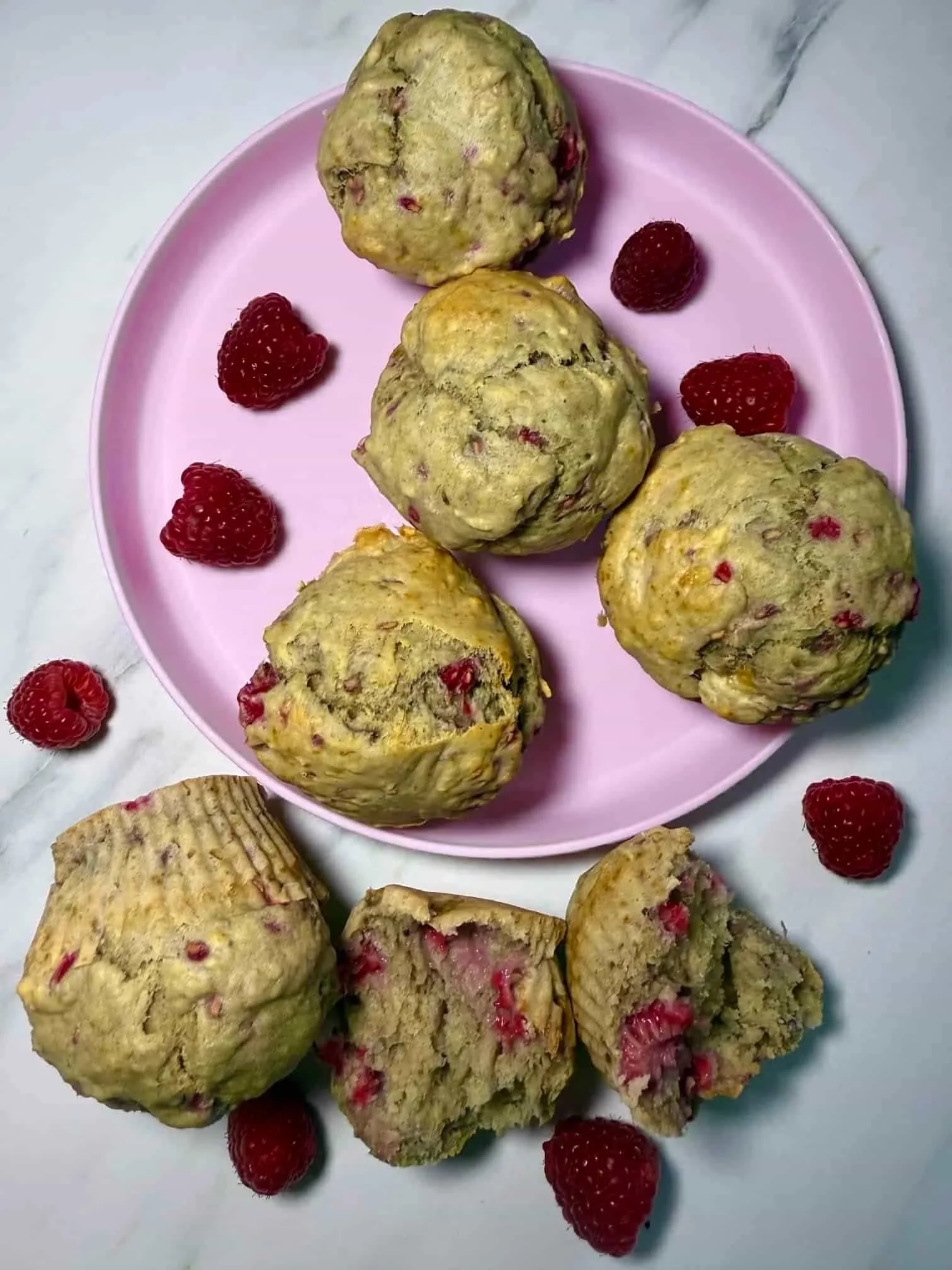 Several baked raspberry muffins served on pink toddler plate with fresh raspberries