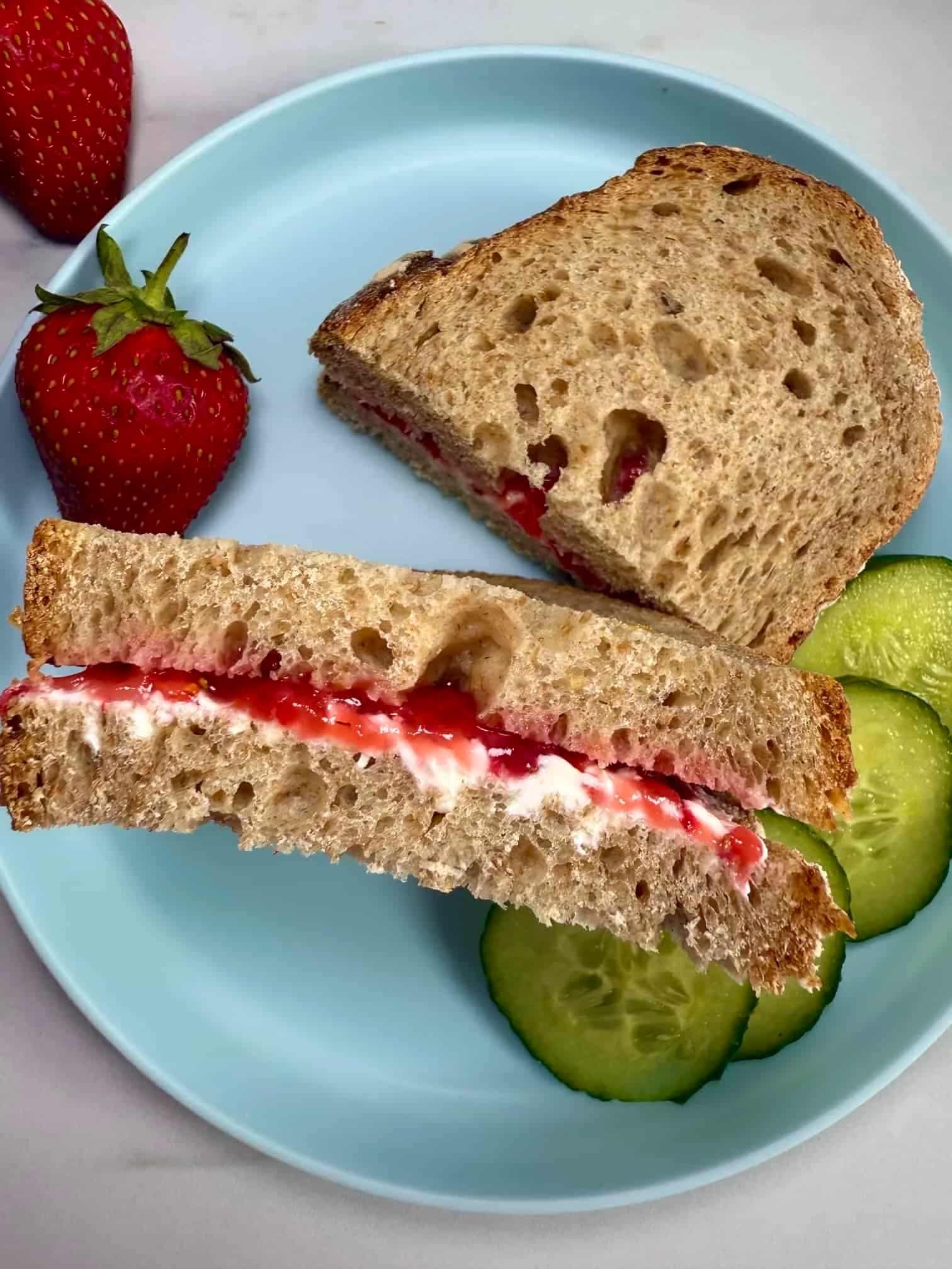 Slices of bread sandwiched together with smashed strawberries and cream cheese and served with slices of cucumber