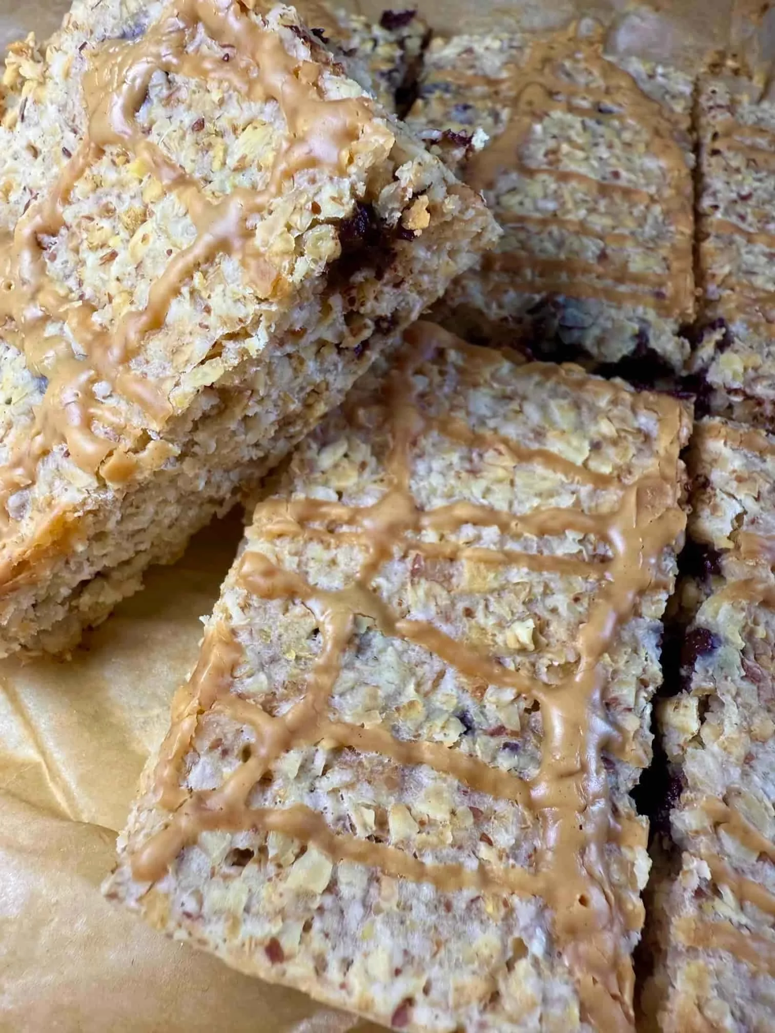 Several baked chocolate chip flapjacks with peanut butter drizzle arranged stacked on a serving board