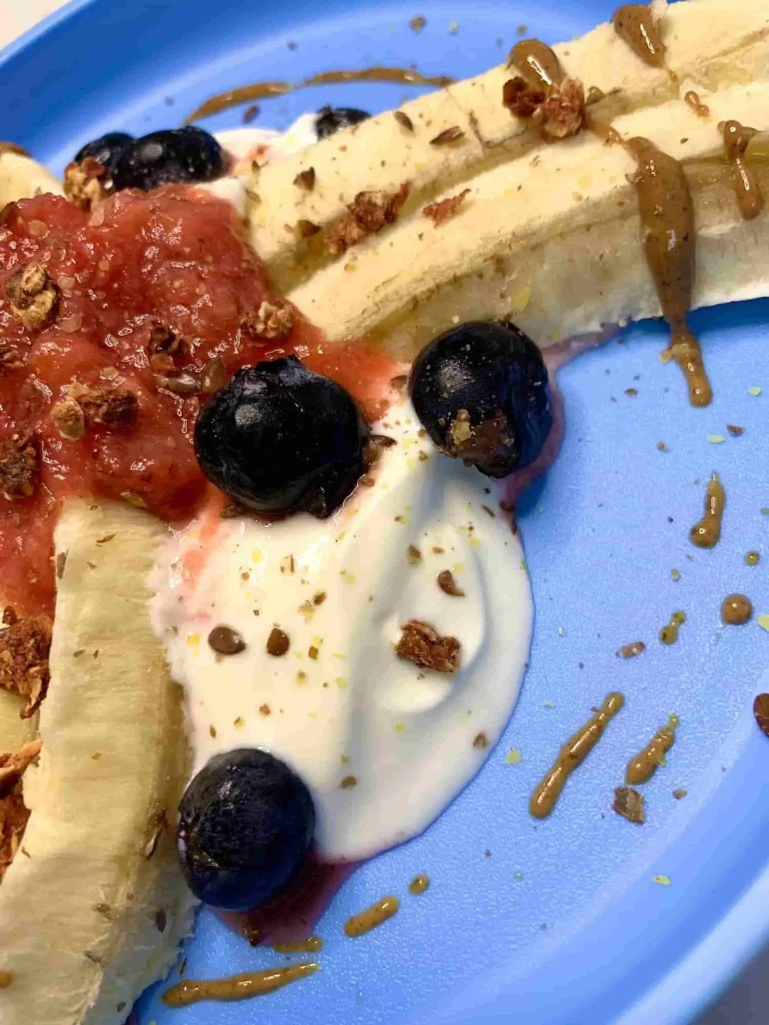 Close up of banana split dessert served with yogurt, berries and peanut butter