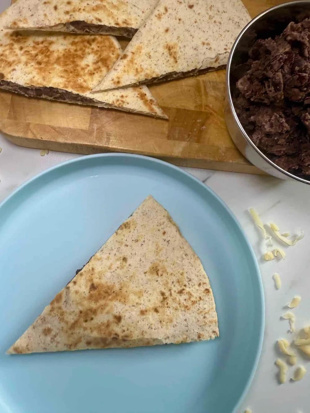 Cooked veggie quesadilla cut into triangles and served on board together with a bowl of the bean filling
