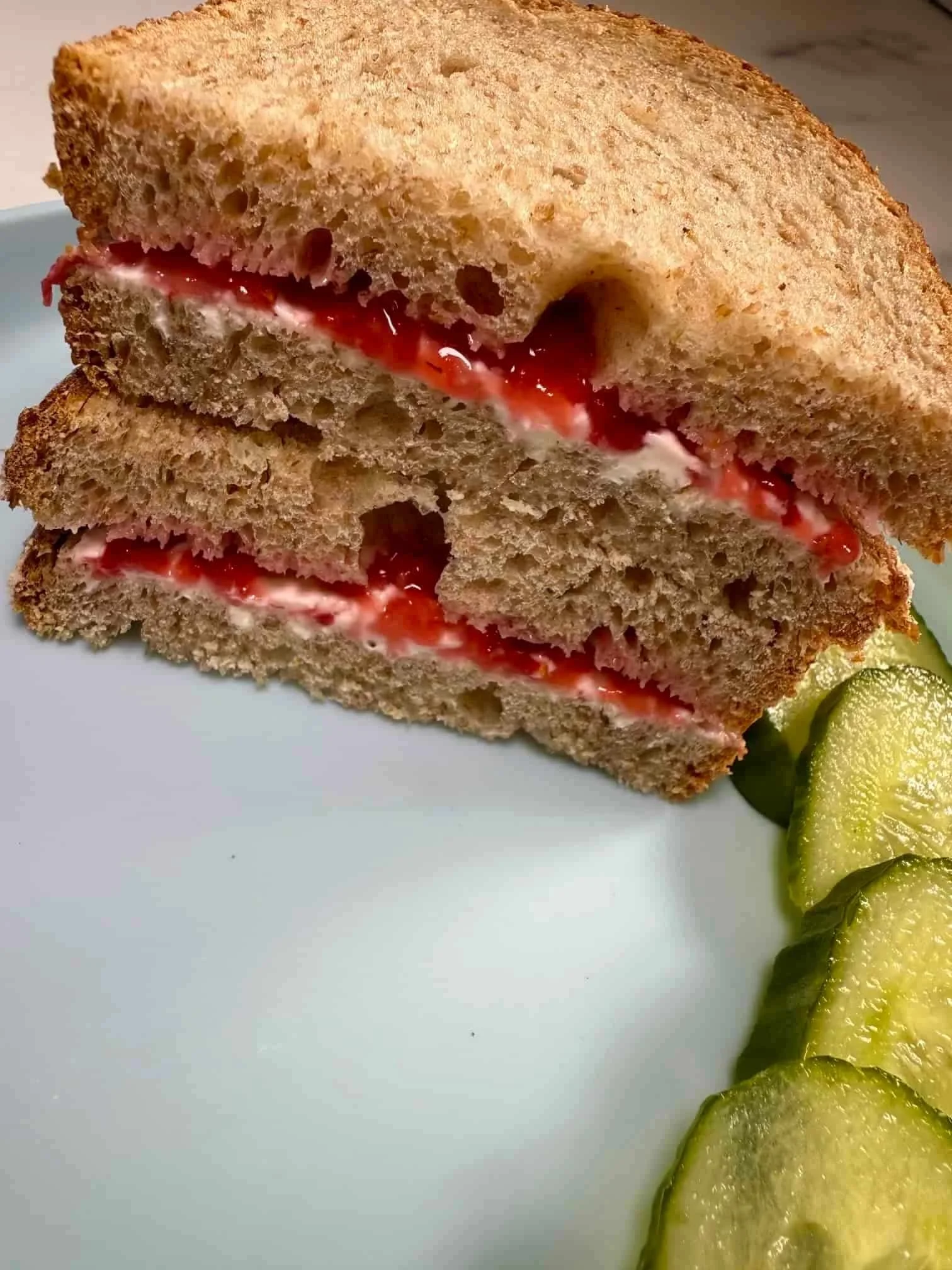 Slices of bread sandwiched together with smashed strawberries and cream cheese and served with slices of cucumber