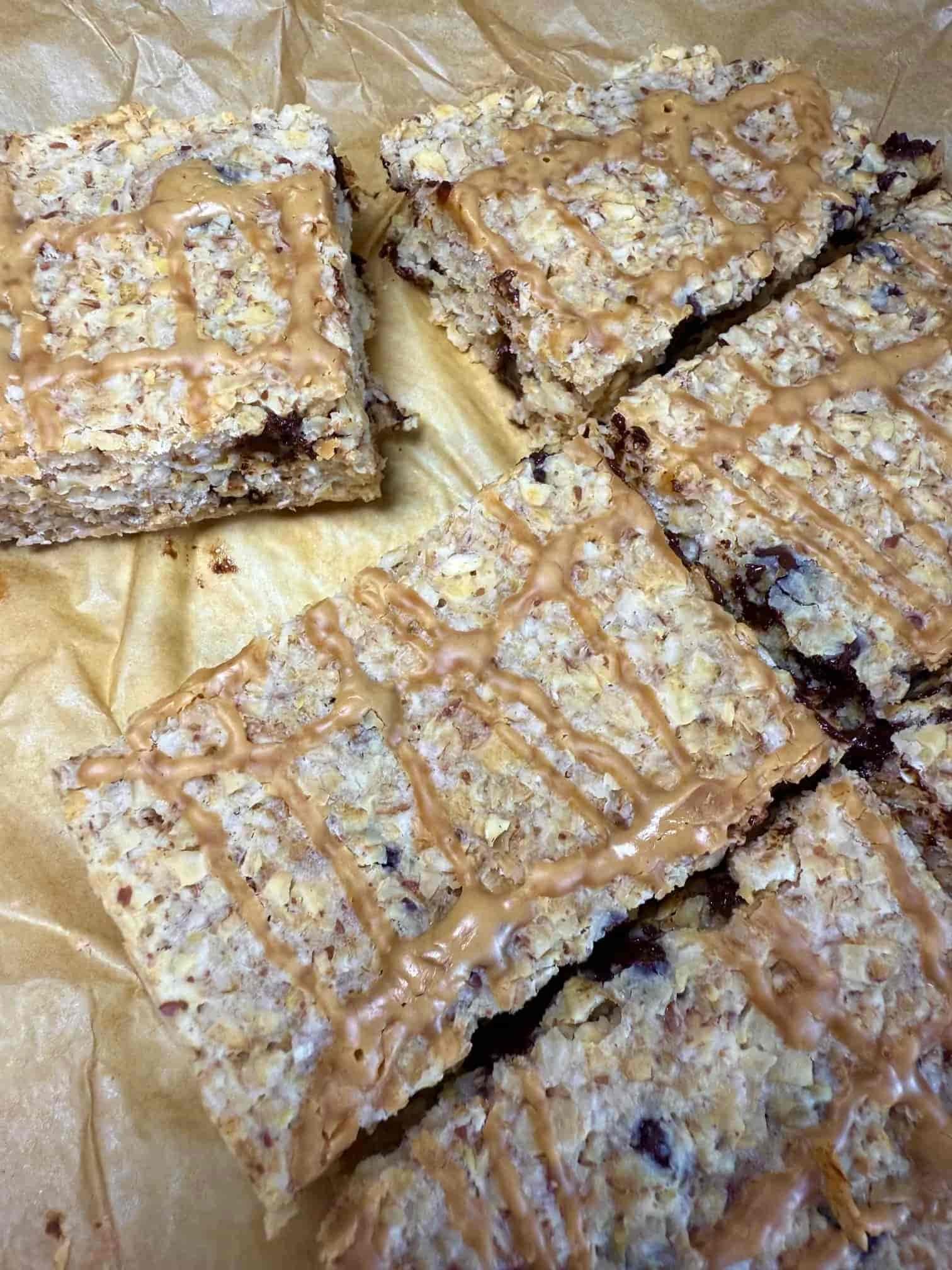 Several baked chocolate chip flapjacks with peanut butter drizzle arranged stacked on a serving board