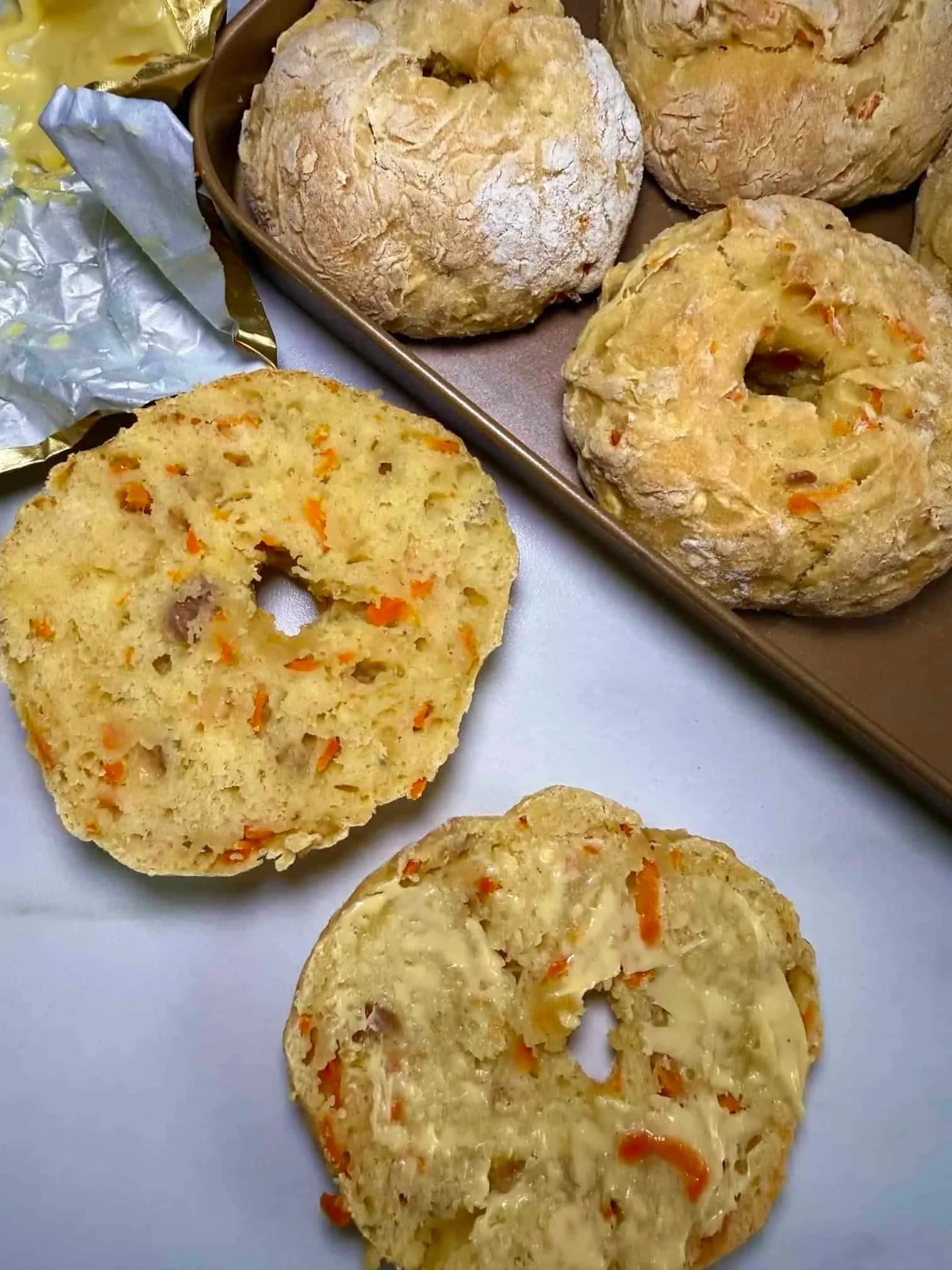 A baked ABC bagel on a baking tray and one cut in half with butter spread on top