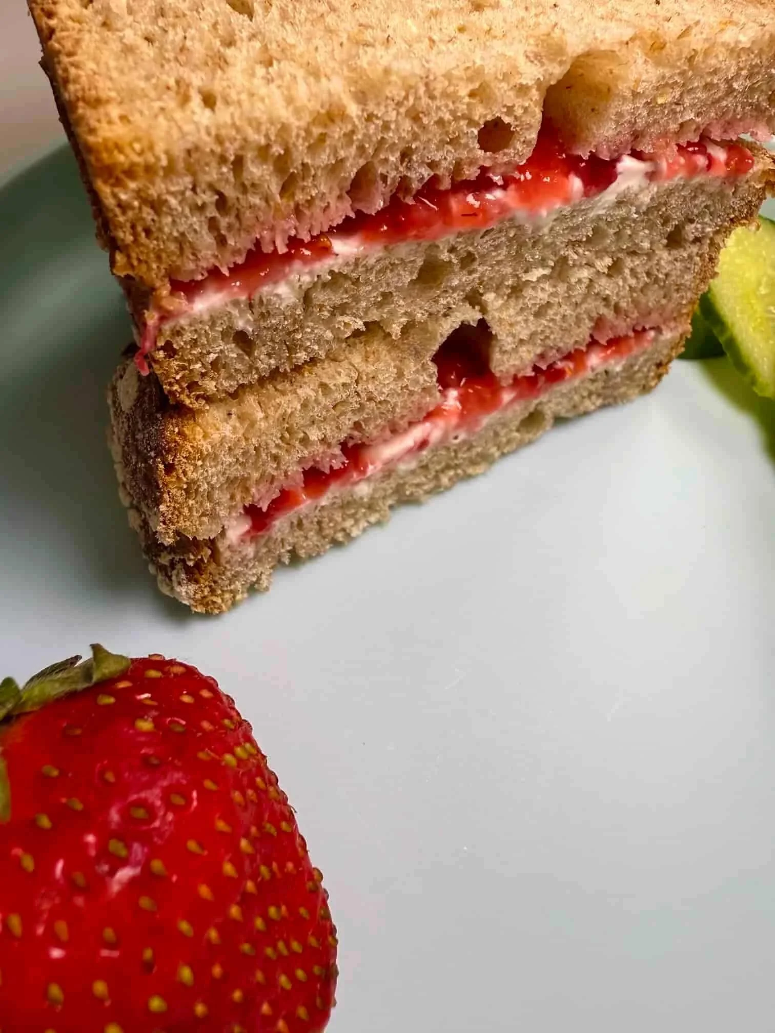 Slices of bread sandwiched together with smashed strawberries and cream cheese and served with slices of cucumber