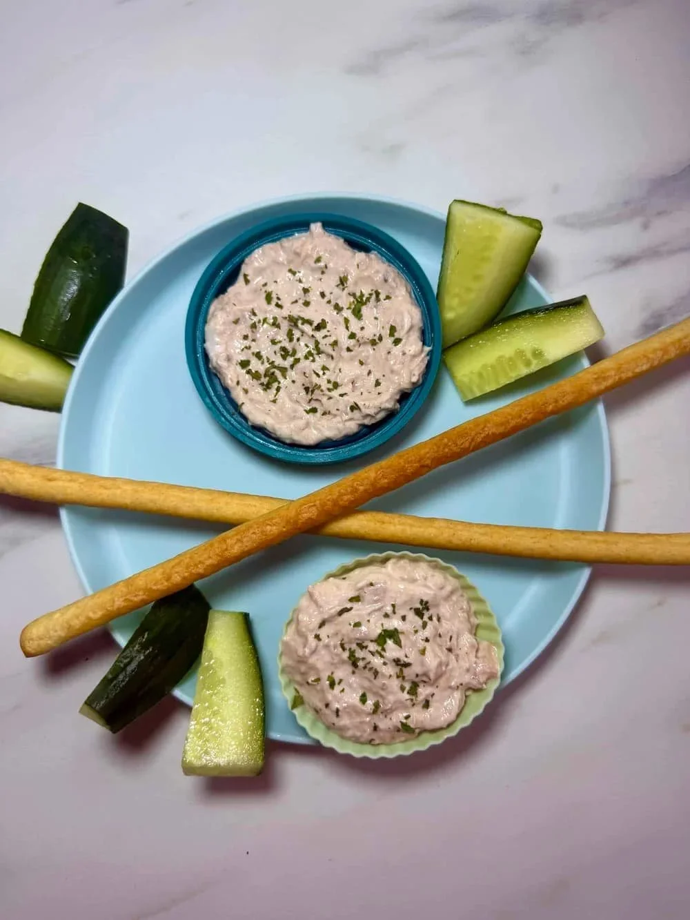 Cream cheese and tuna dip served in silicone case with breadsticks and sticks of cucumber