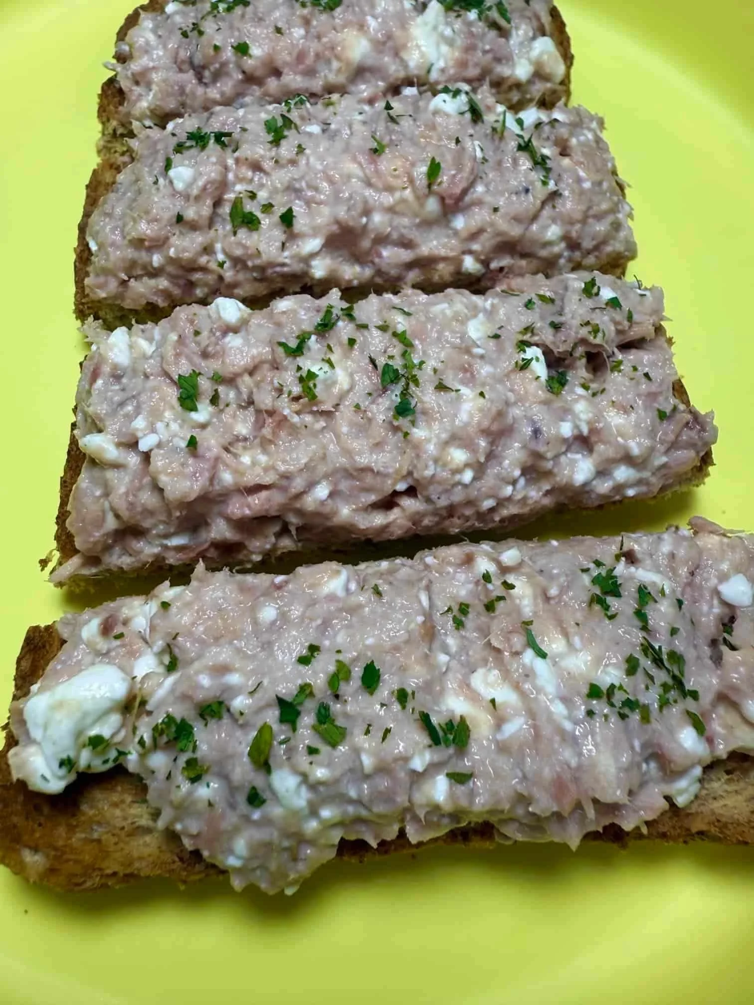 A tuna and cottage cheese topping spread on toast, garnished with parsley and served on toddler plate