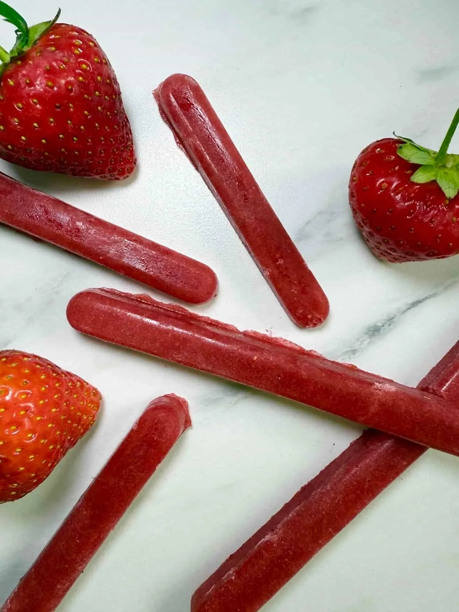 Five sticks of frozen strawberry puree served with fresh strawberries