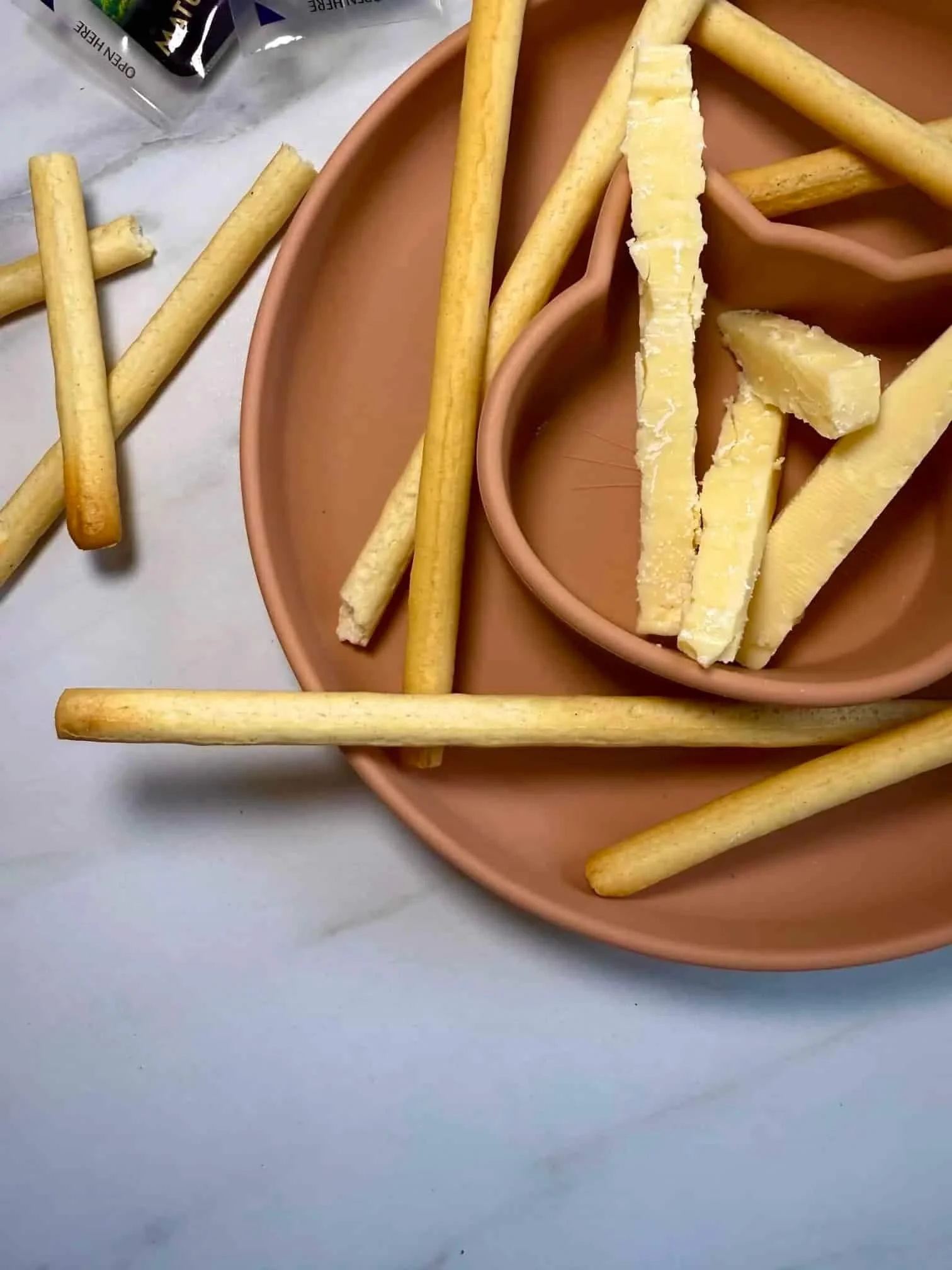 Breadsticks and fingers of cheese together with some cucumber presented on a toddler dish