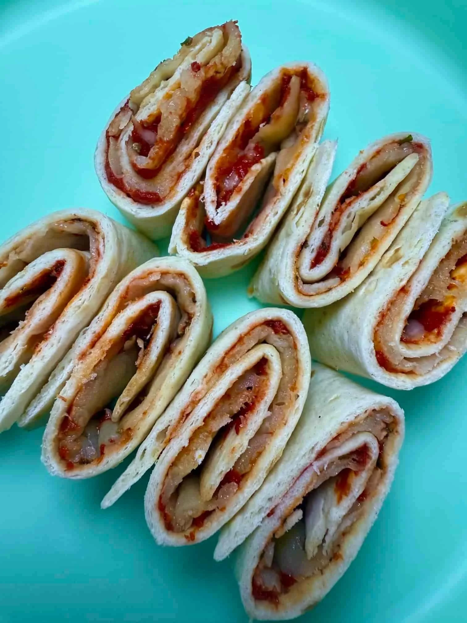 Several tortilla pizza roll-ups, sliced and standing on serving dish