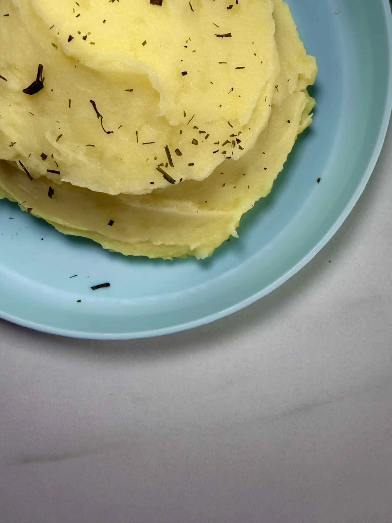 A serving of homemade mashed potato on a toddler plate sprinkled with chives