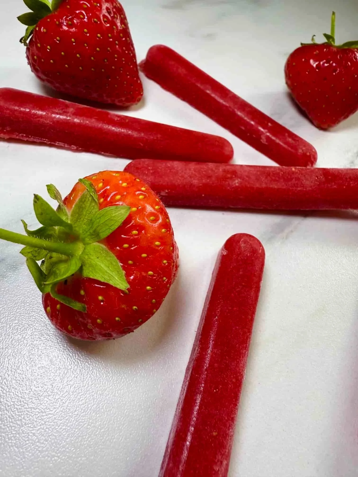Four sticks of frozen strawberry puree served with fresh strawberries