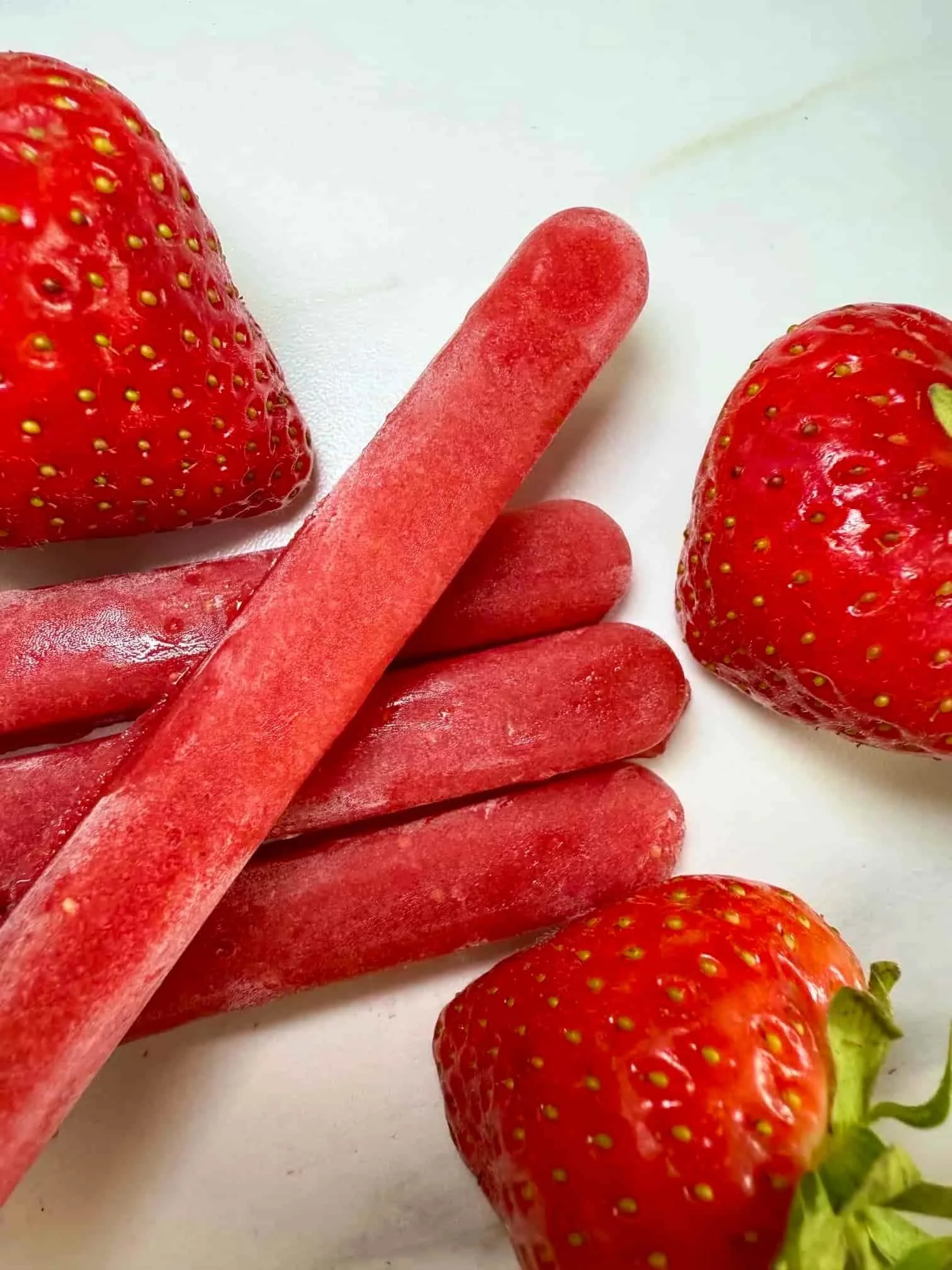 Four sticks of frozen strawberry puree served with fresh strawberries