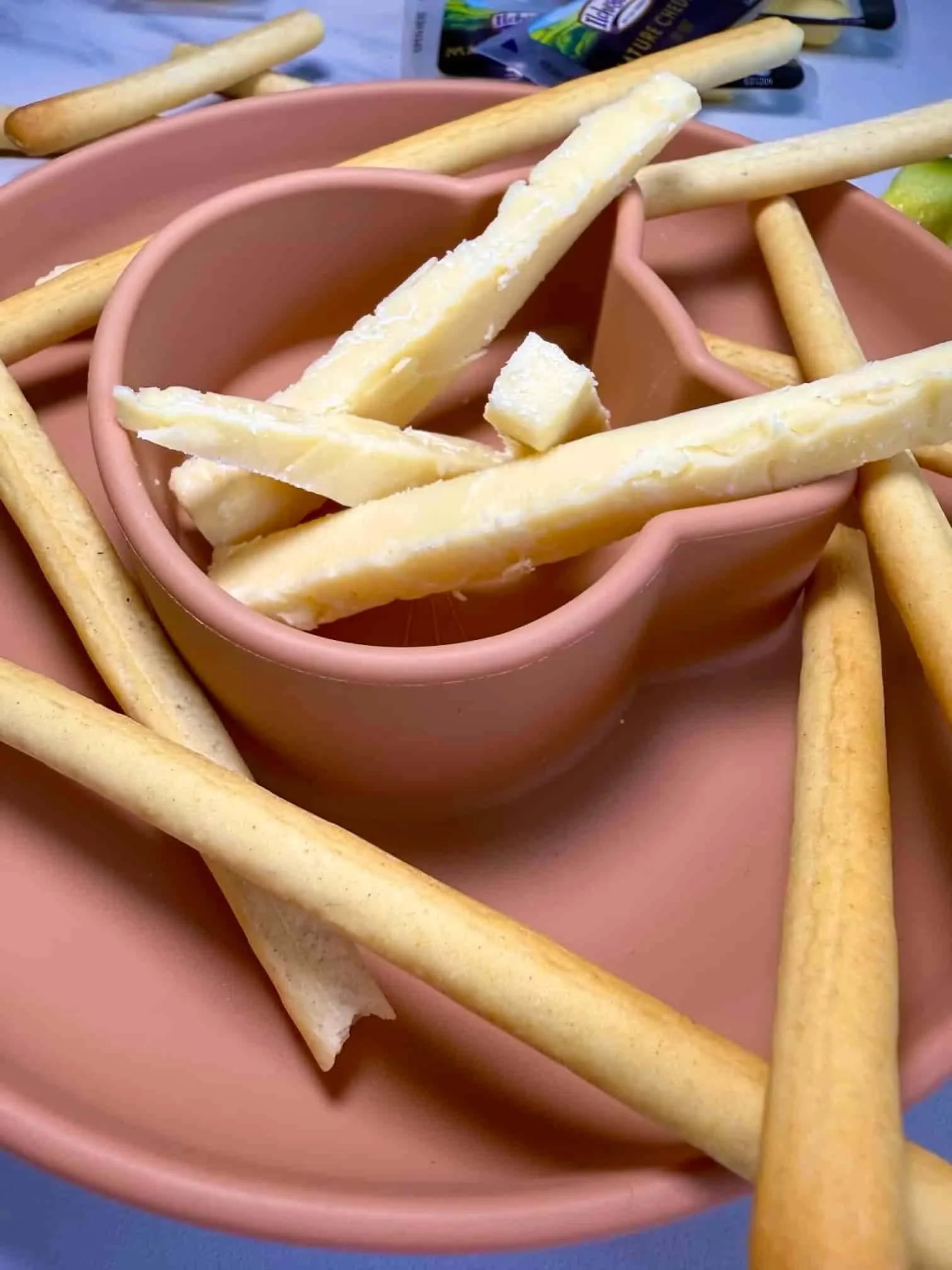 Breadsticks and fingers of cheese together with some cucumber presented on a toddler dish