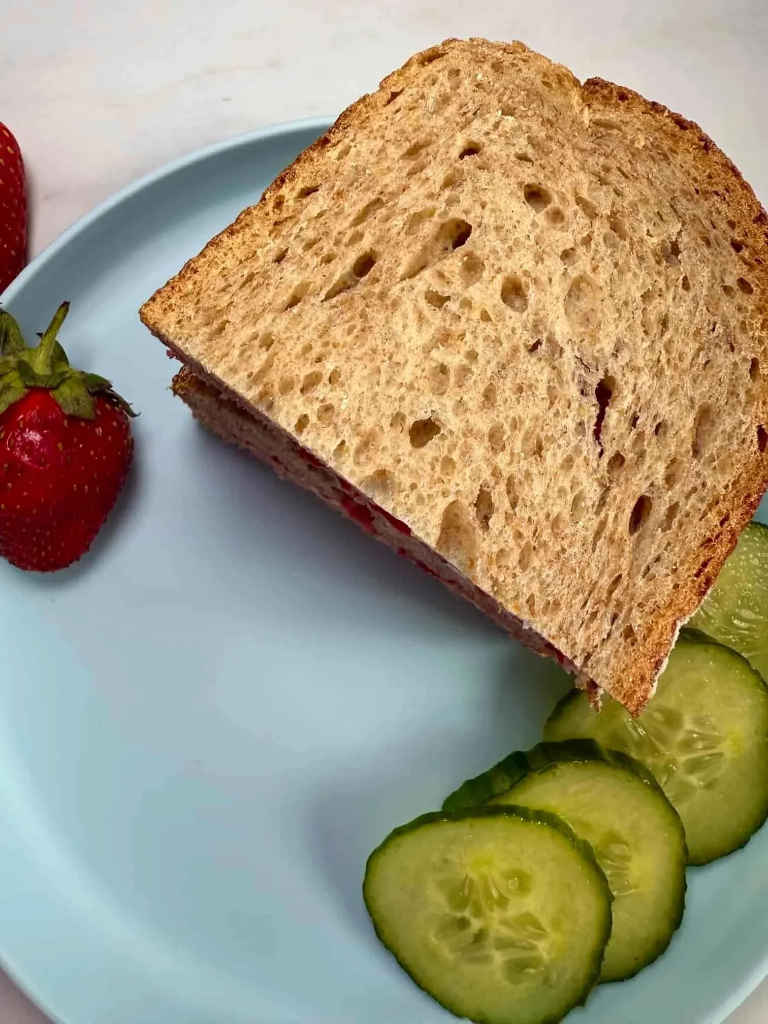 Slices of bread sandwiched together with smashed strawberries and cream cheese and served with slices of cucumber