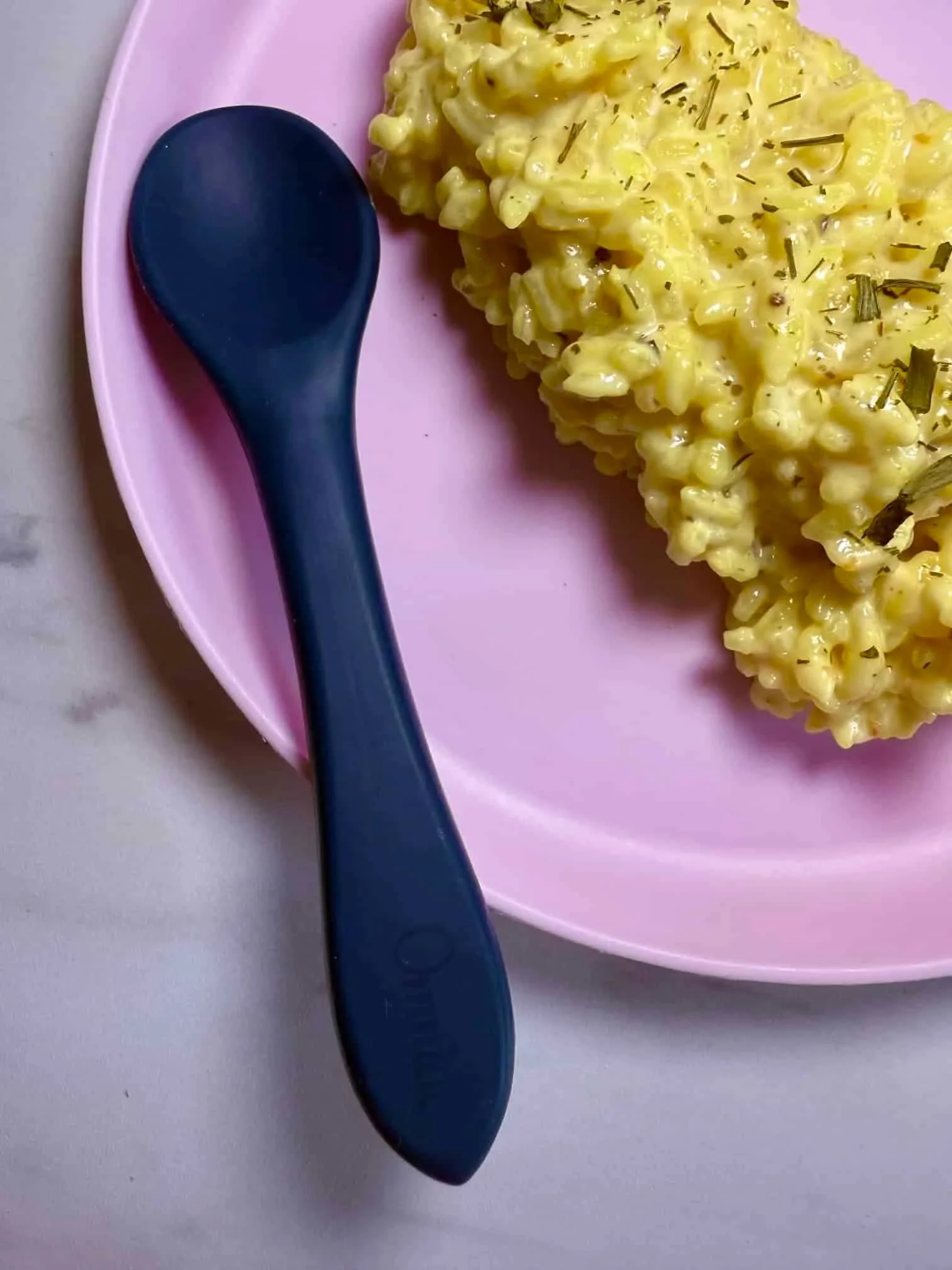 A cooked portion of risotto in a creamy sauce sprinkled with dried chives and served on a toddler plate