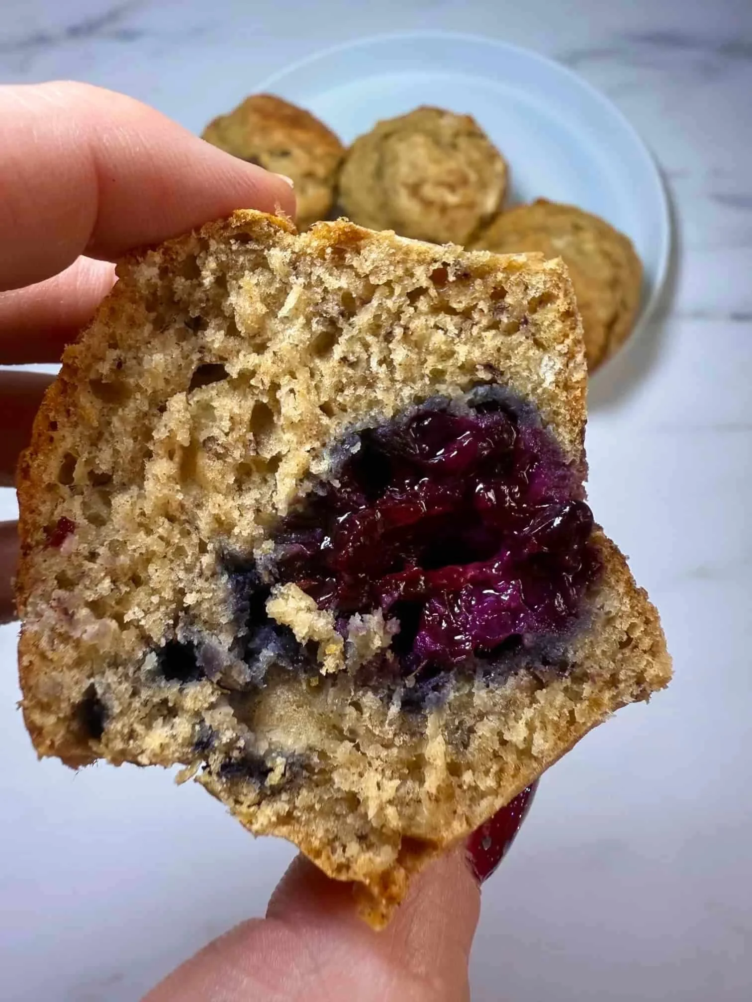 Several baked banana and blackberry muffins on a serving plate, some whole and some cut in half to show the fruit inside
