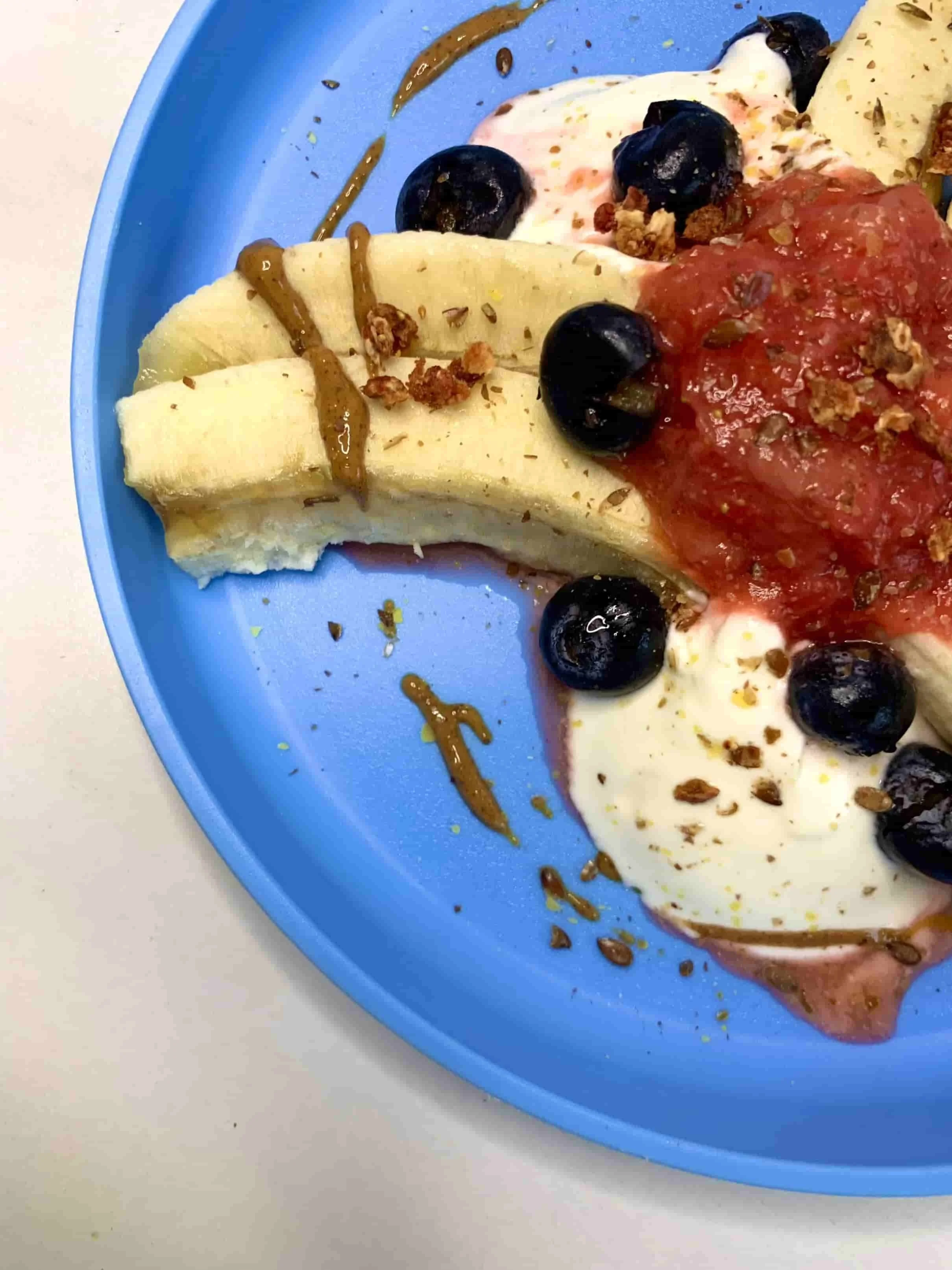 Side view of banana split dessert served with yogurt, berries and peanut butter