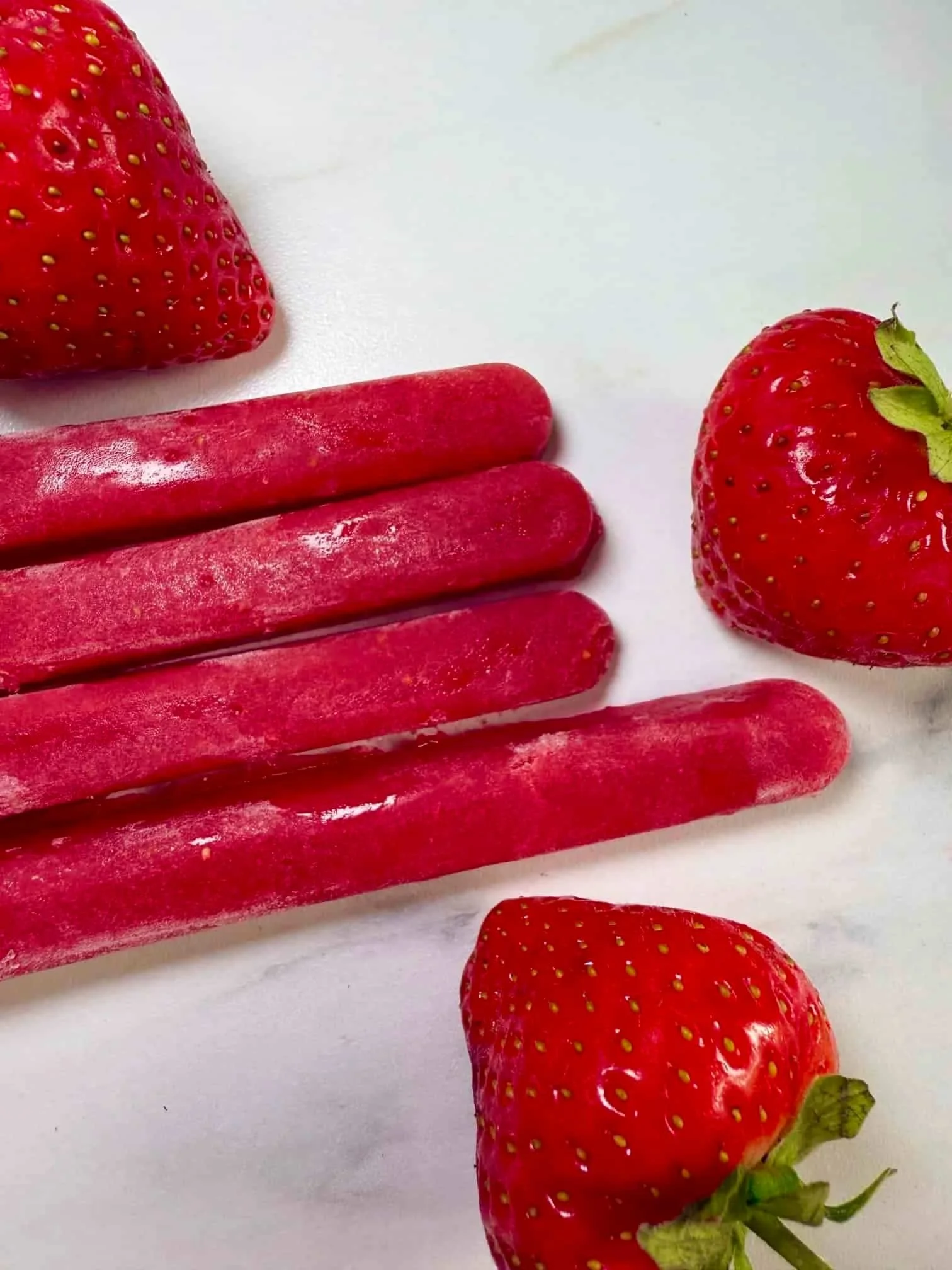 Four sticks of frozen strawberry puree served with fresh strawberries