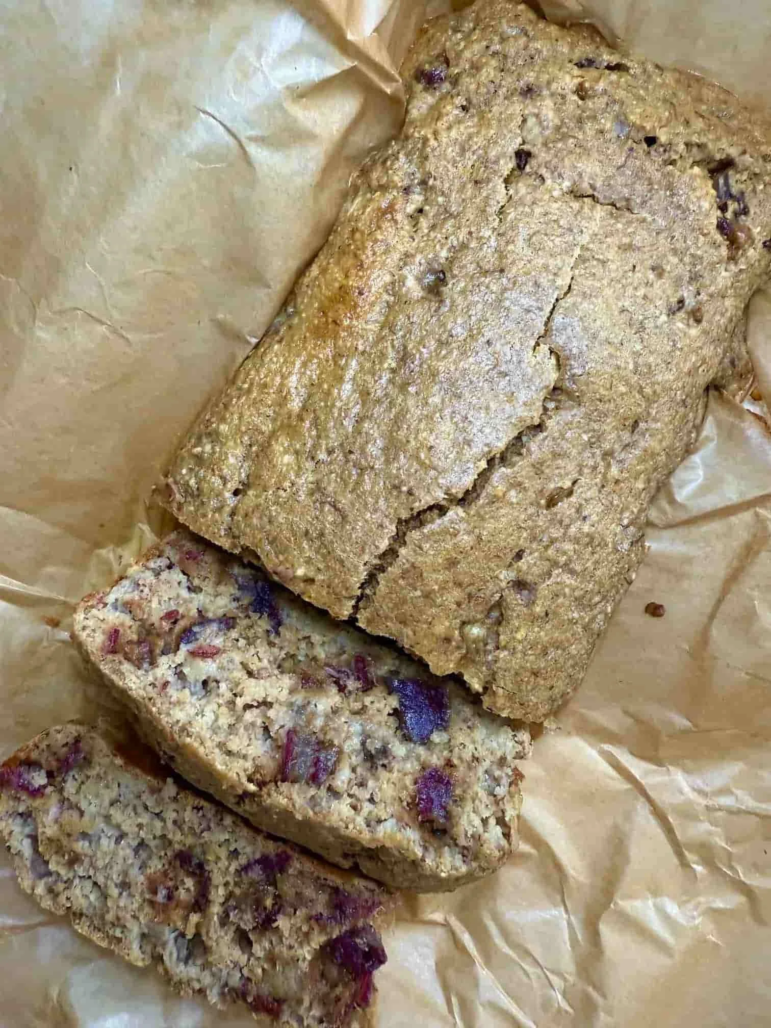 A cooked date and banana loaf with two slices cut from the main cake on parchment paper
