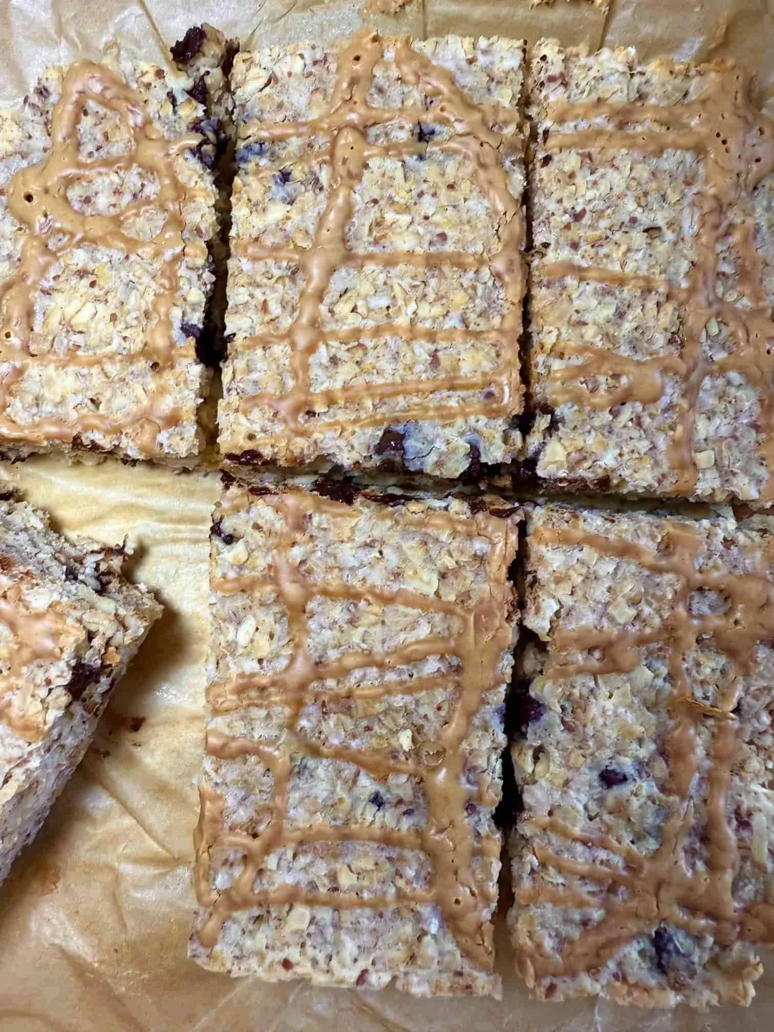 Several baked chocolate chip flapjacks with peanut butter drizzle arranged stacked on a serving board