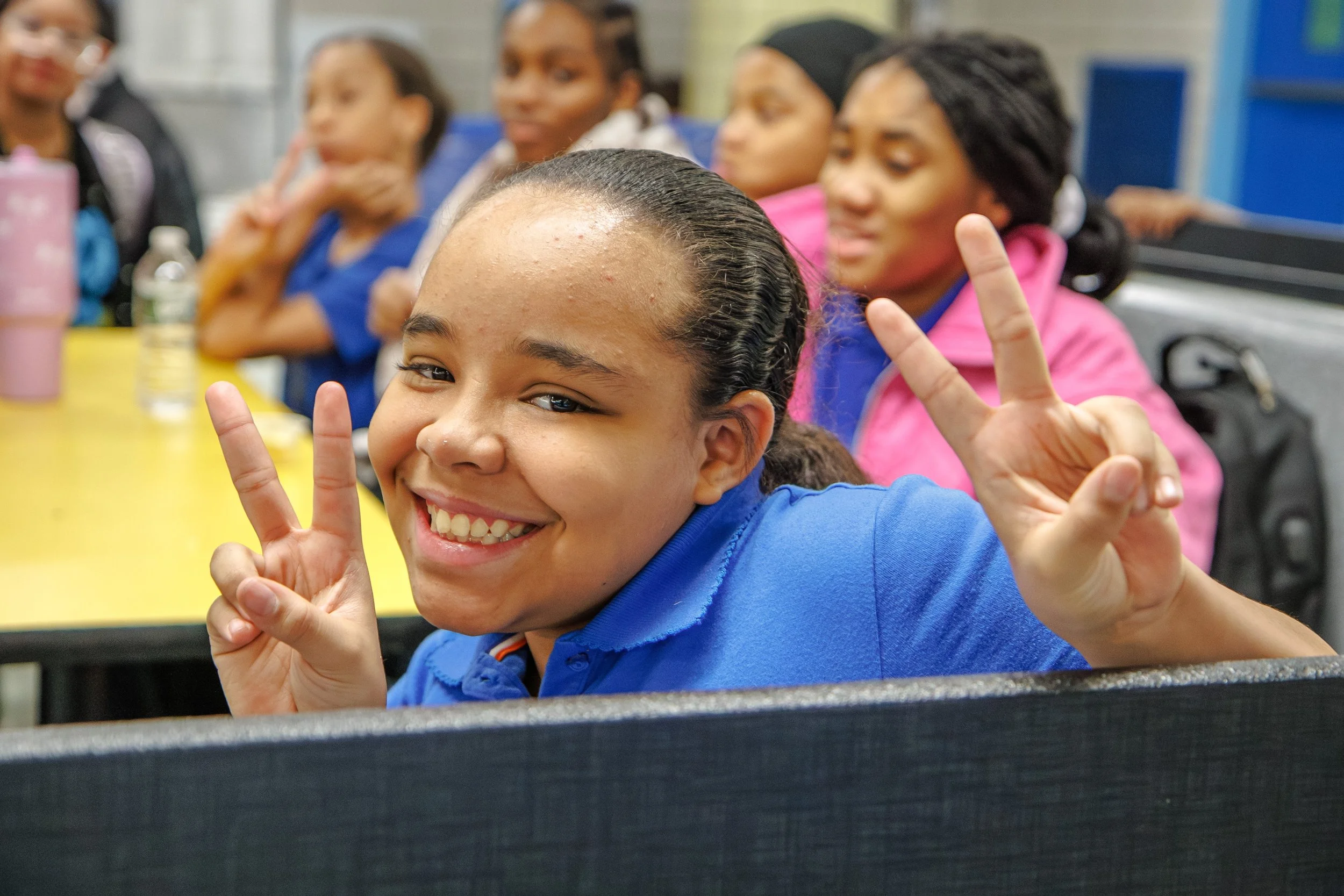 
Smiling student flashing double peace signs while sitting at a table.