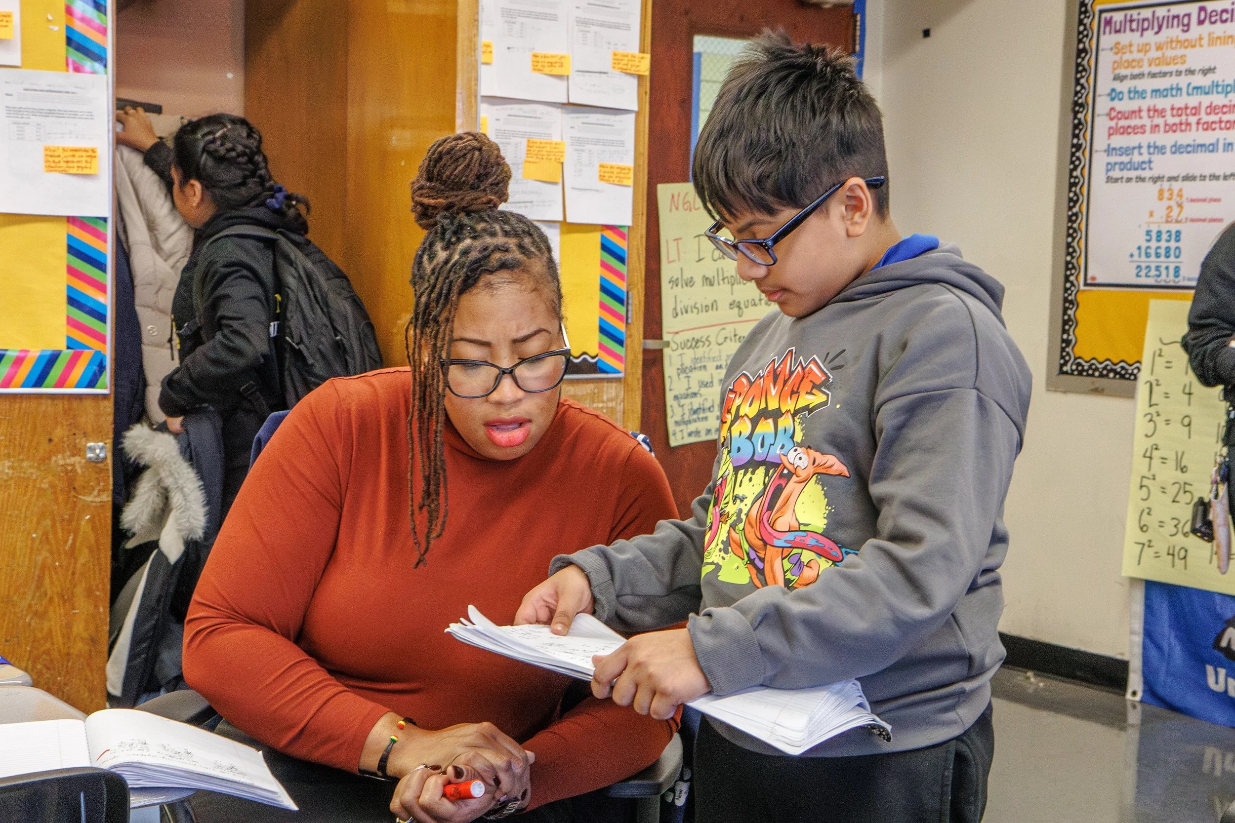 Teacher reviewing a workbook with a student in a classroom.