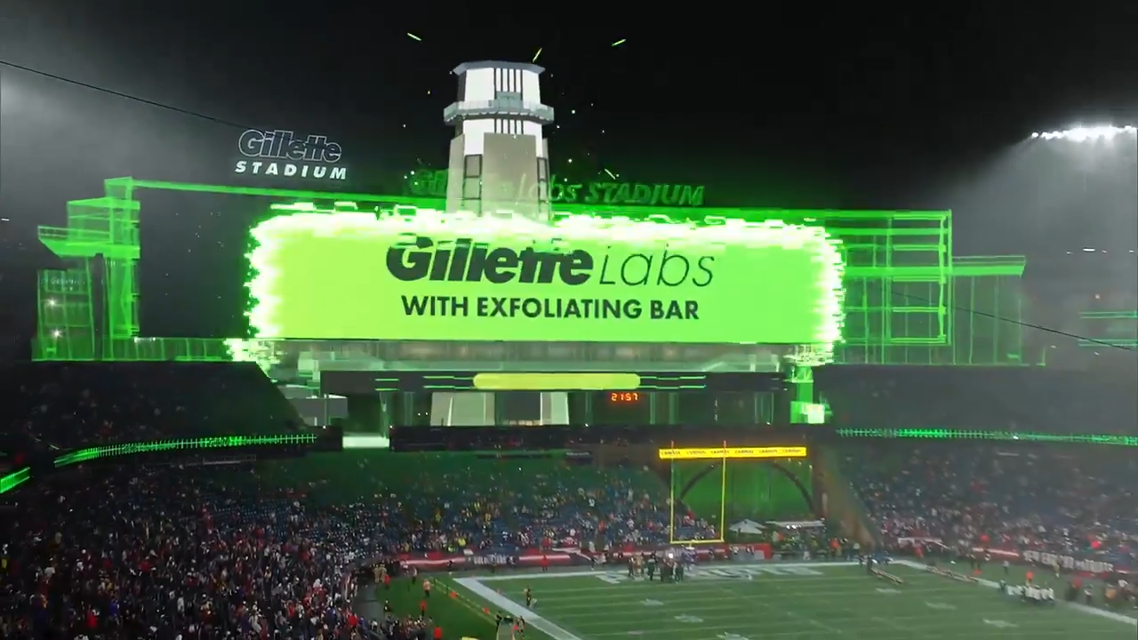 Football stadium virtual set with Gillette Labs ad on a large digital screen, featuring bright green text, stadium lights, and spectators, created with Unreal Engine and Pixotope in a real-time virtual production pipeline.
