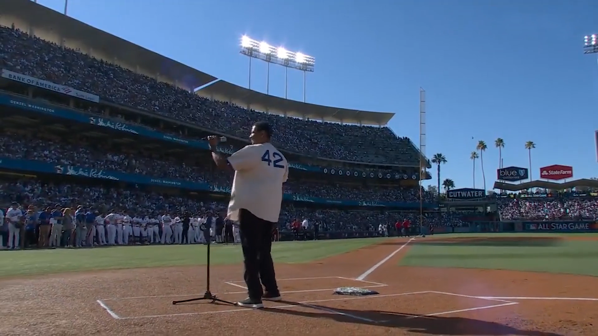 Denzel Washington wearing a white baseball jersey with number 42, standing at home plate in a stadium with bright lights and a cheering crowd, created with Unreal Engine and Pixotope in a real-time virtual production pipeline.
