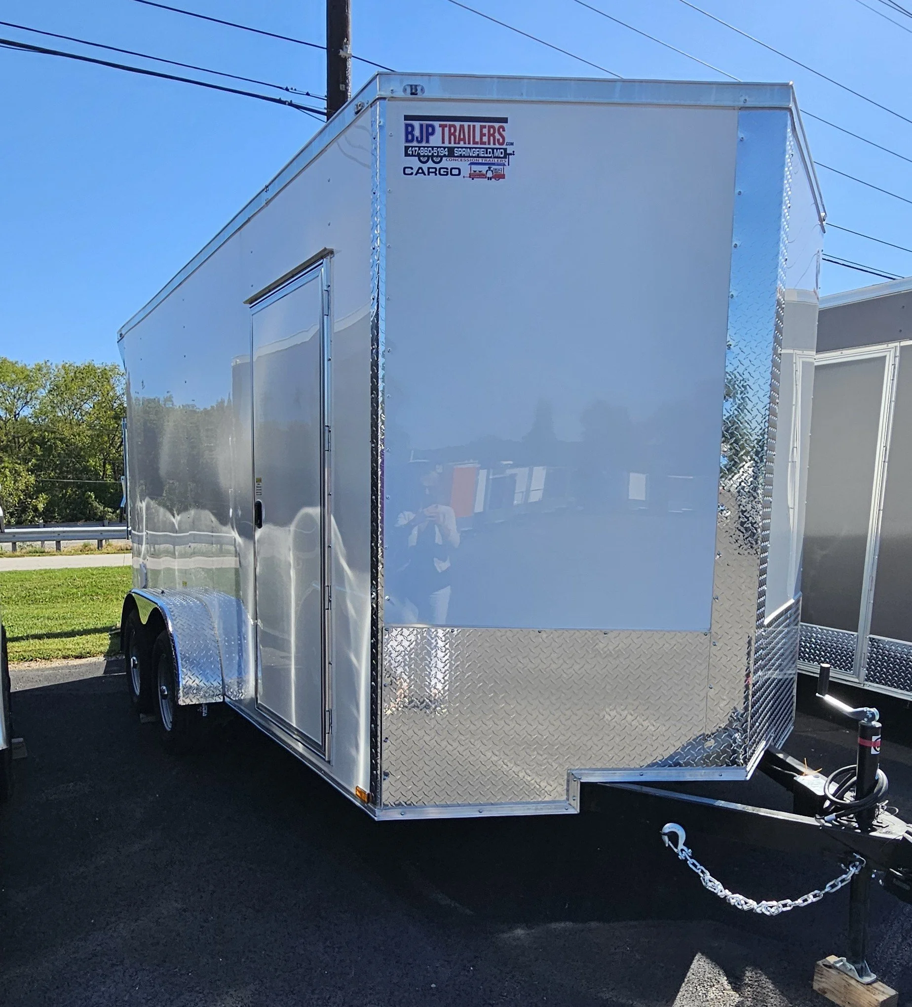 White enclosed cargo trailer looking from the tongue down the left side with a side door in front of the wheel well.