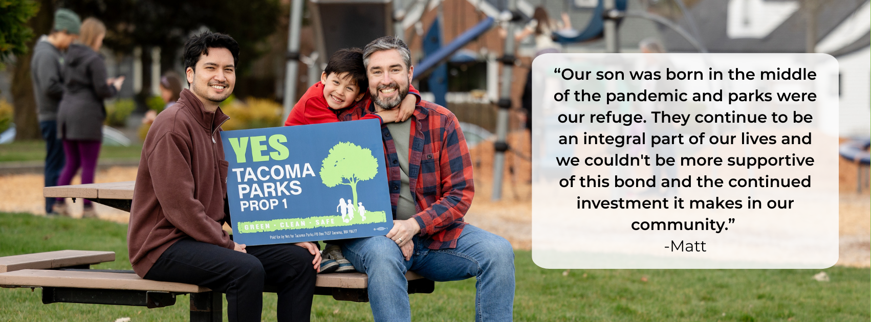 Three people, two men and a boy, sitting on a park bench holding a sign supporting Tacoma parks. The boy is hugging one of the men. In the background, other people are in a park, some using their phones. The park has grassy areas, trees, and playground equipment.