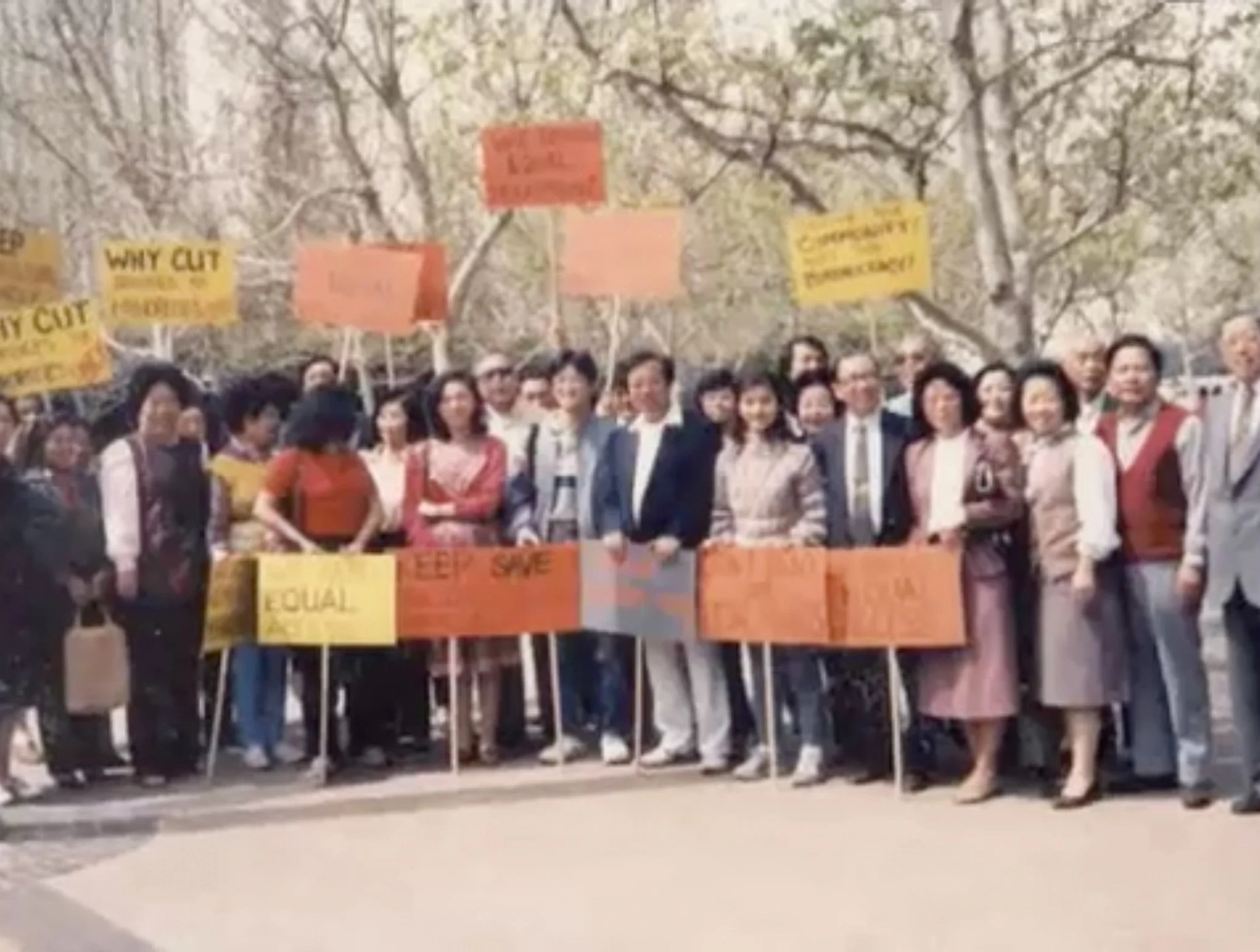 A group of diverse people standing outdoors, holding protest signs with slogans about gender equality and women's rights, under leafless trees.