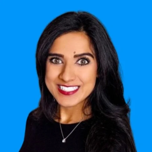 Portrait of a woman with long black hair, smiling, wearing a black top and a necklace, against a blue background.