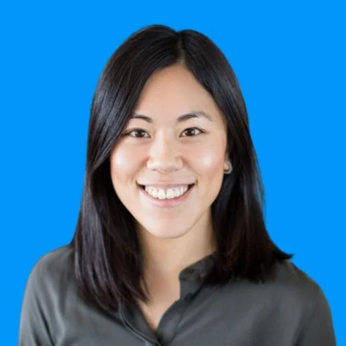 Portrait of smiling Asian woman with black hair wearing a dark gray top against a blue background.