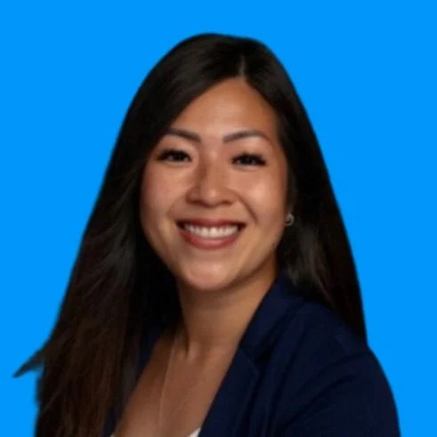 A smiling woman with long dark hair wearing a navy blazer against a blue background.