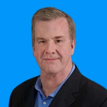 Headshot of a middle-aged man with short light brown hair, wearing a dark blazer over a blue collared shirt, against a solid blue background.