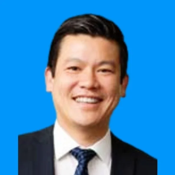 A smiling man in a suit and tie against a blue background.